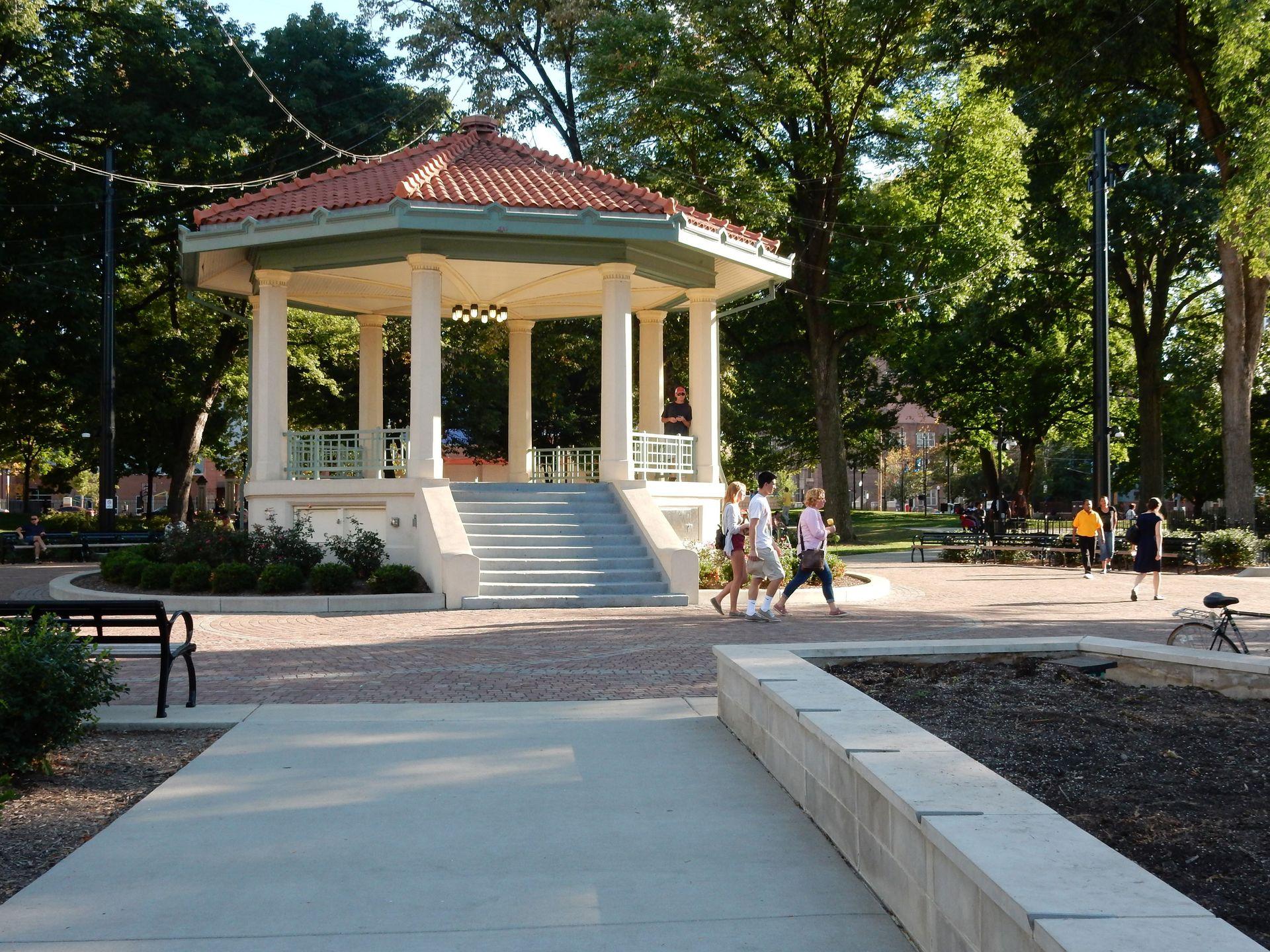 The central gazebo in Washington Park. It is white with a red roof and hanging lights are coming off of the top.