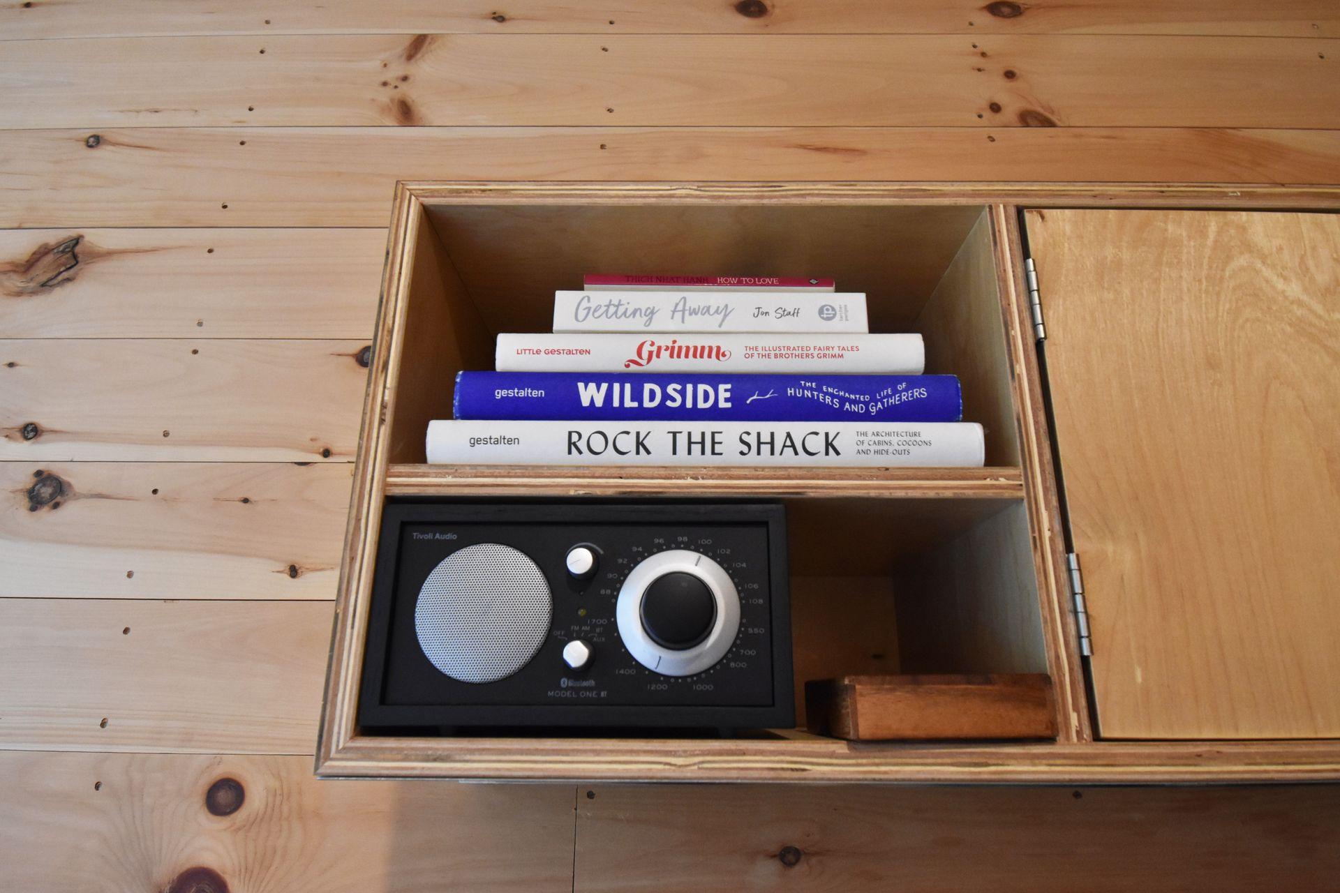 A wooden shelf with a radio and several books inside of the Getaway House cabin.