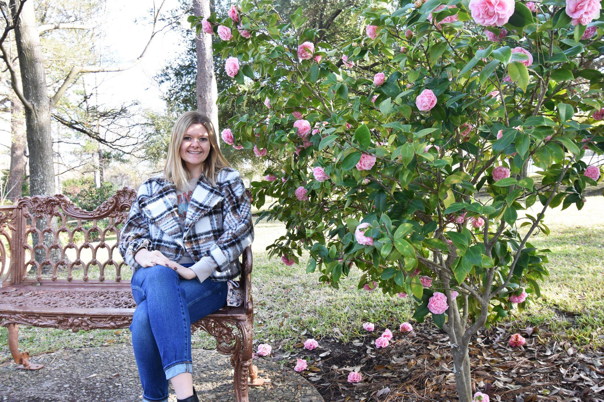 Lydia sitting next to a pink rose bush at the Tyler Rose Garden.