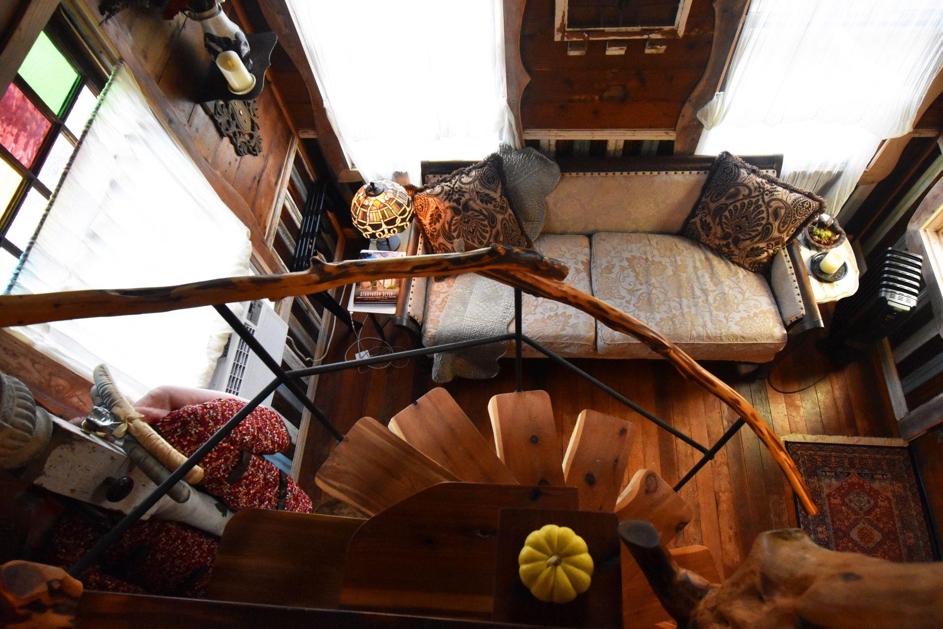 Looking down from the loft in Havenwald. There is a spiral staircase, a vintage-looking couch with pillows, wood details and a stained glass lamp.