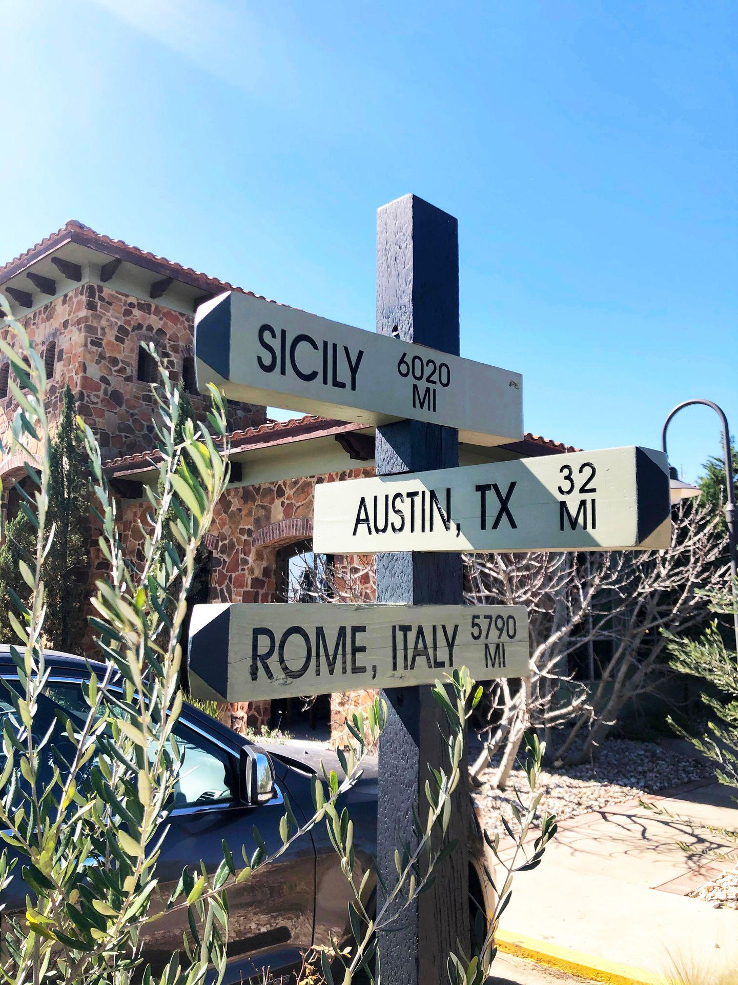 A wooden sign that has the distances from Sicily, Austin and Rome