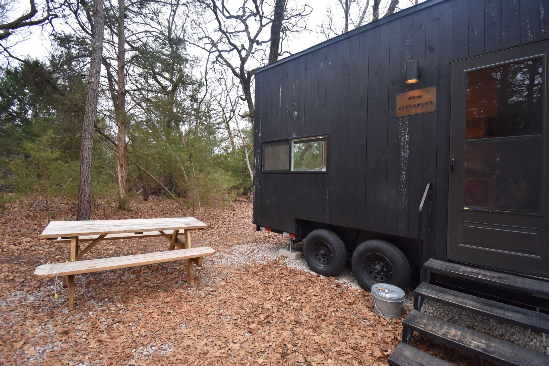 A black cabin on wheel with a picnic table next to it.