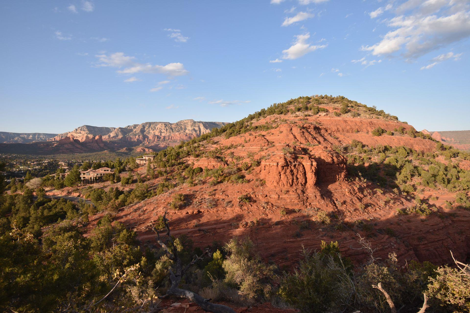 A small orange mountain next to the city of Sedona. There is a larger orange cliff in the distance.