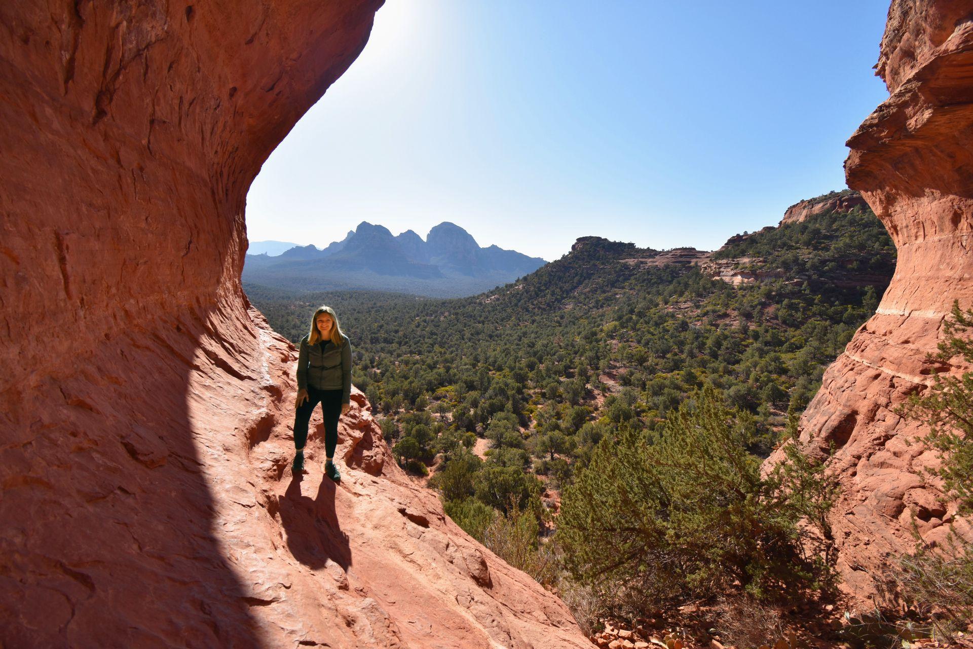 Lydia standing on the edge of Birthing Cave with a view of Sedona in the background.
