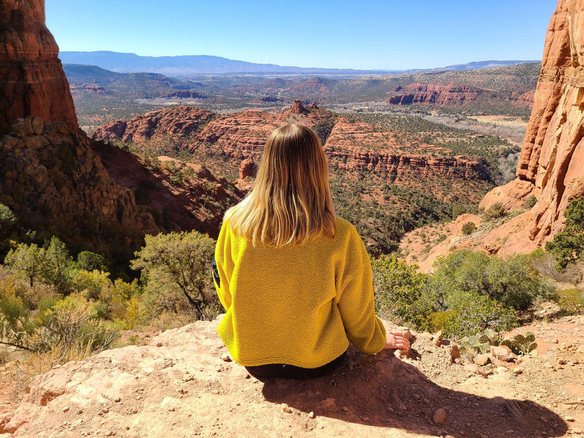 Lydia sitting on a rock face and looking out at red rock views on the Cathedral Rock trail.