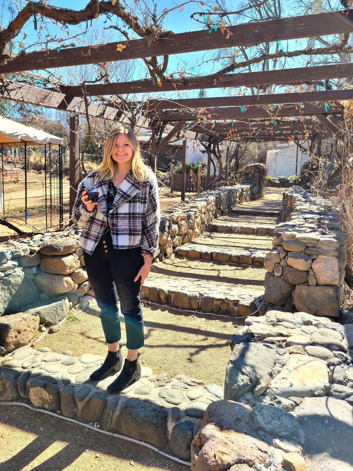 Lydia standing on a pathway at Page Spring Cellars. She holds a glass of wine and is wearing a plaid coat.