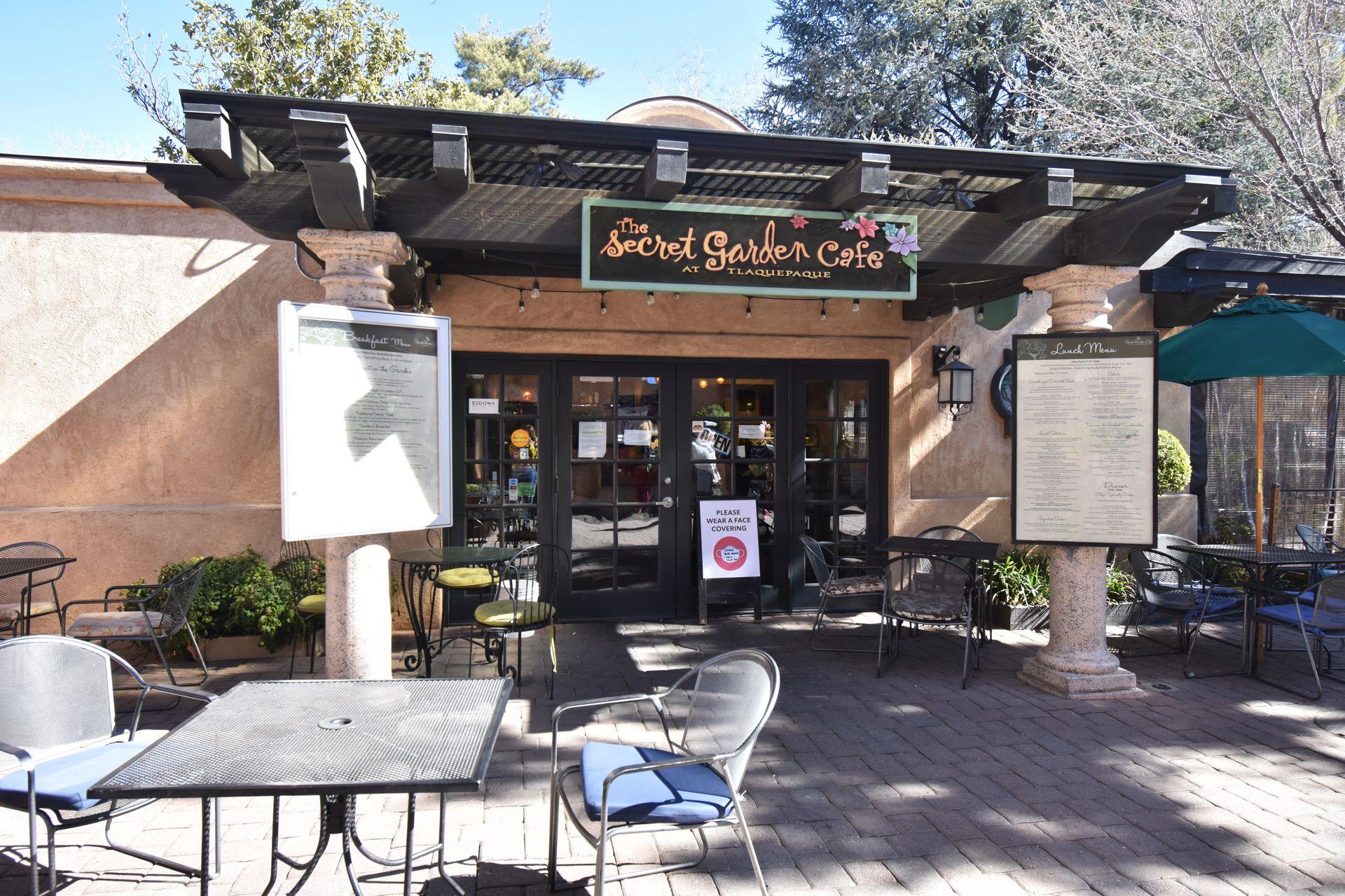 The exterior of The Secret Garden Cafe. There are menus and a table in front of the building.