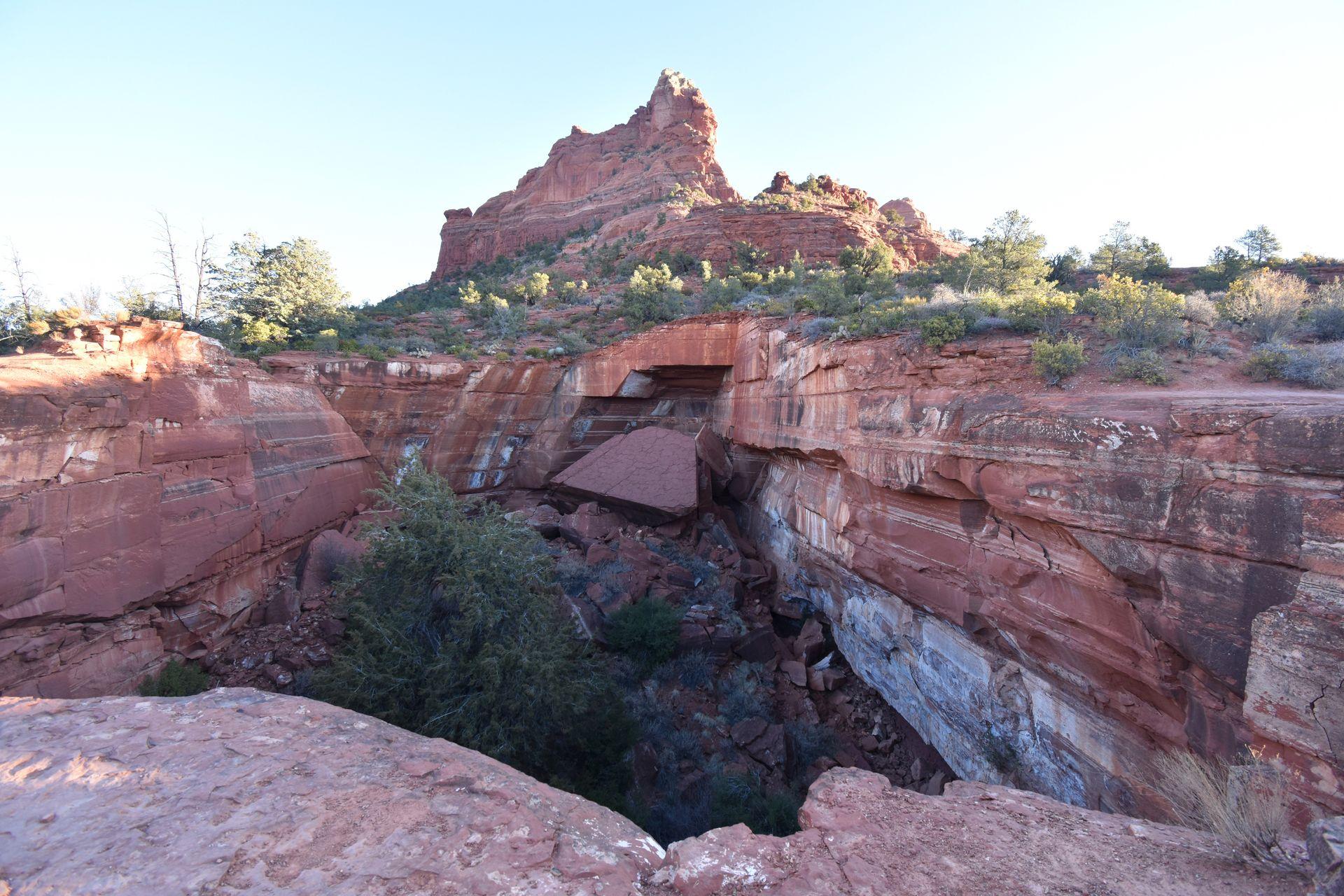 A giant hole surrounded by orange rocks. There are green trees at the bottom of the hole.