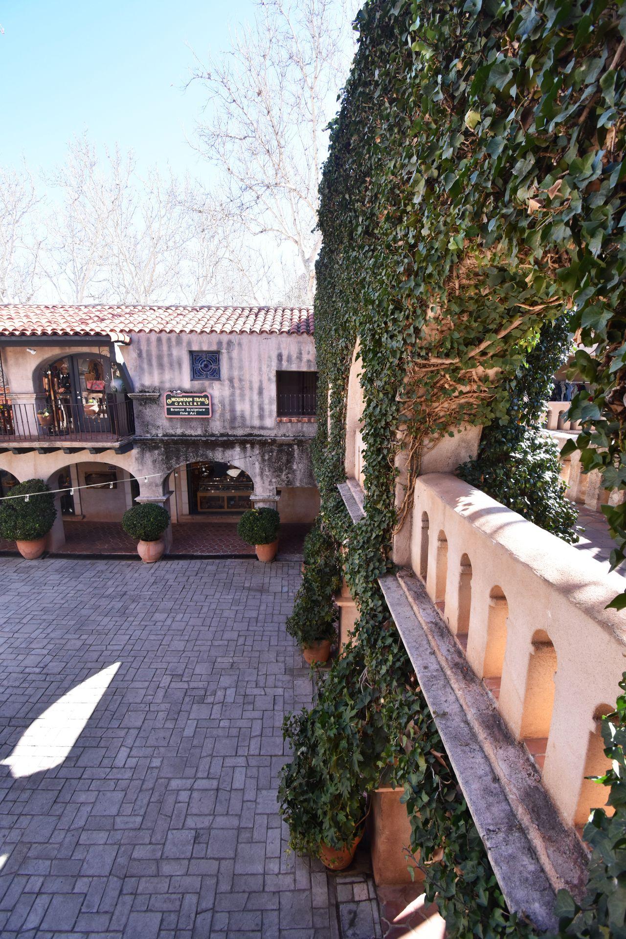 An outdoor shopping area with arches and a wall covered in green vines. This view looks down at Tlaquepaque Arts and Shopping Village from an upper balcony.