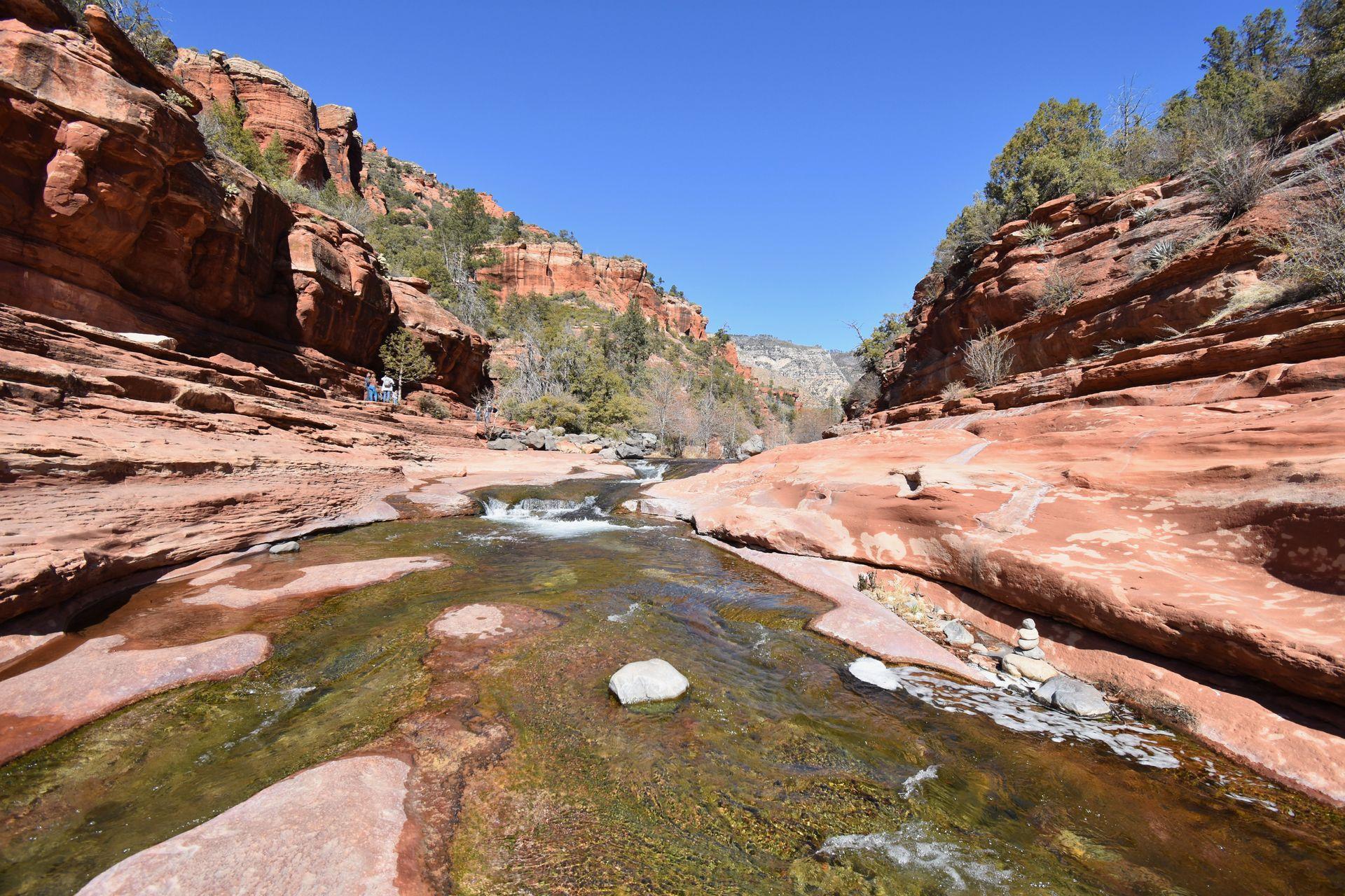 A stream of water flowing through an orange rock canyon at Slide Rock Park.