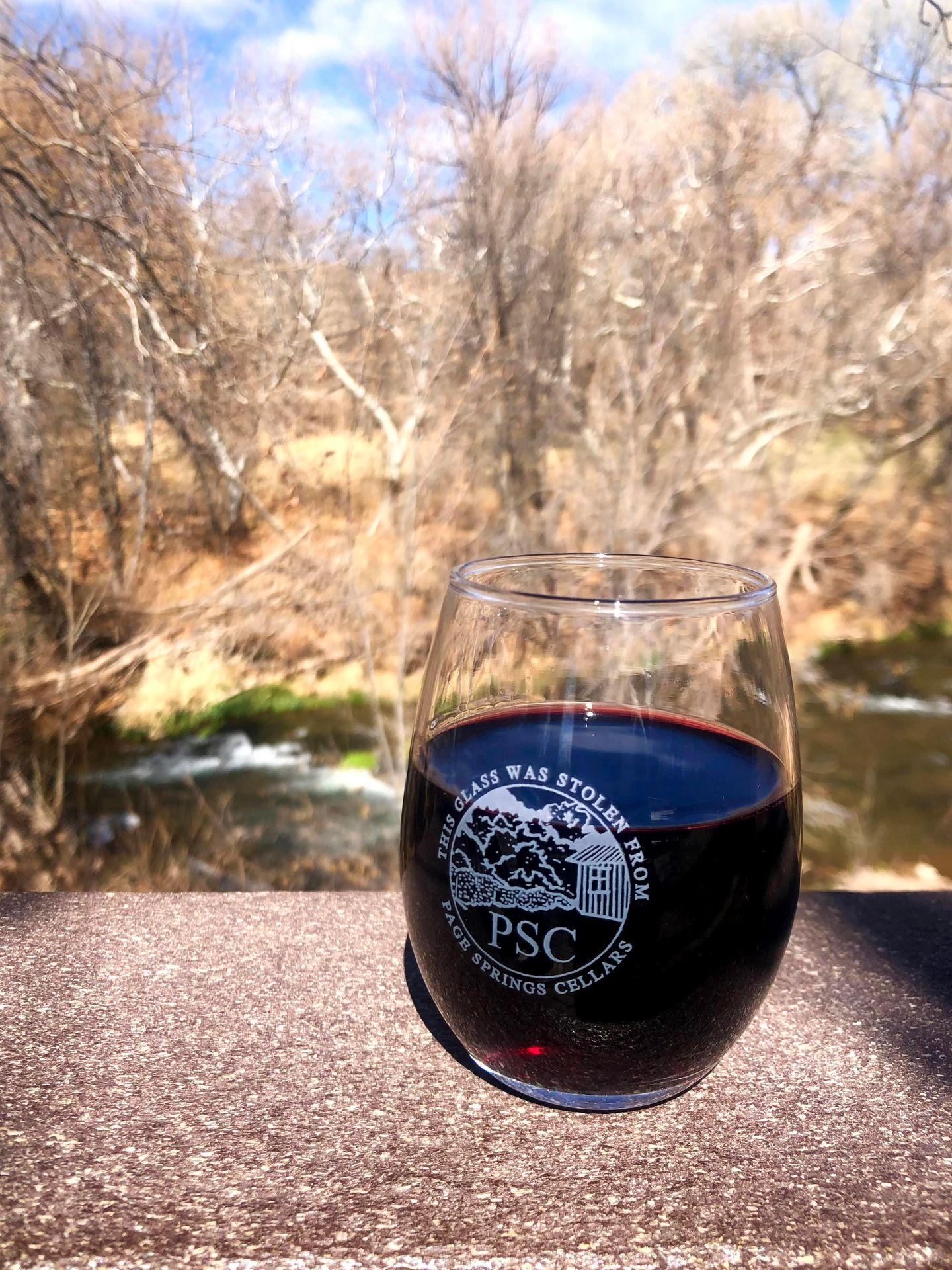 A glass of red wine sitting on a ledge with views of a creek behind it.