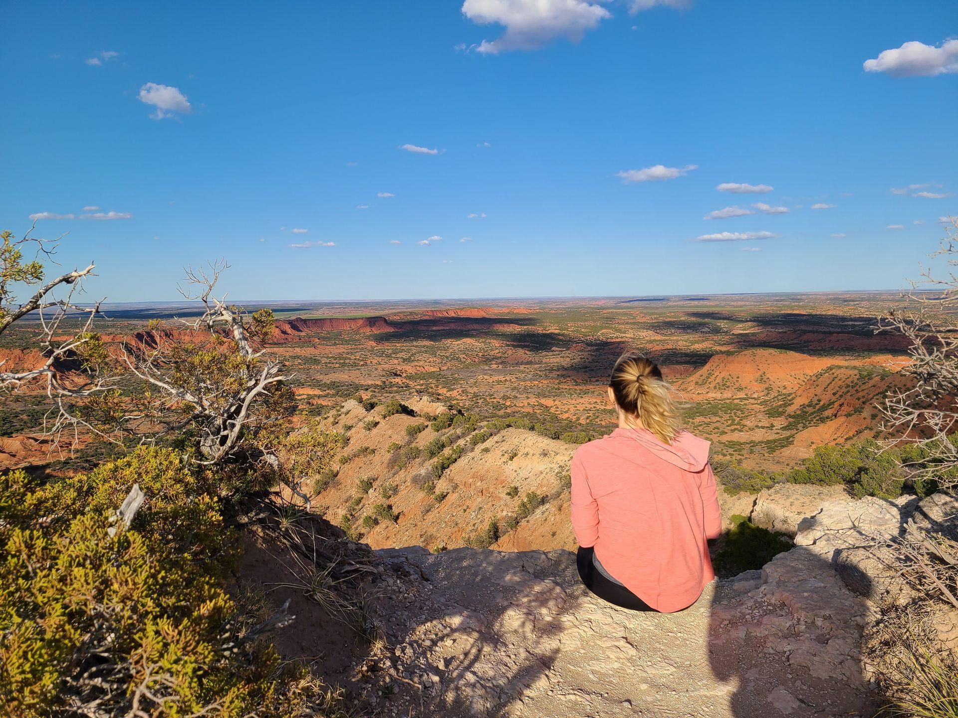 Lydia sitting on a ledge and looking out a canyon with orange rock views.