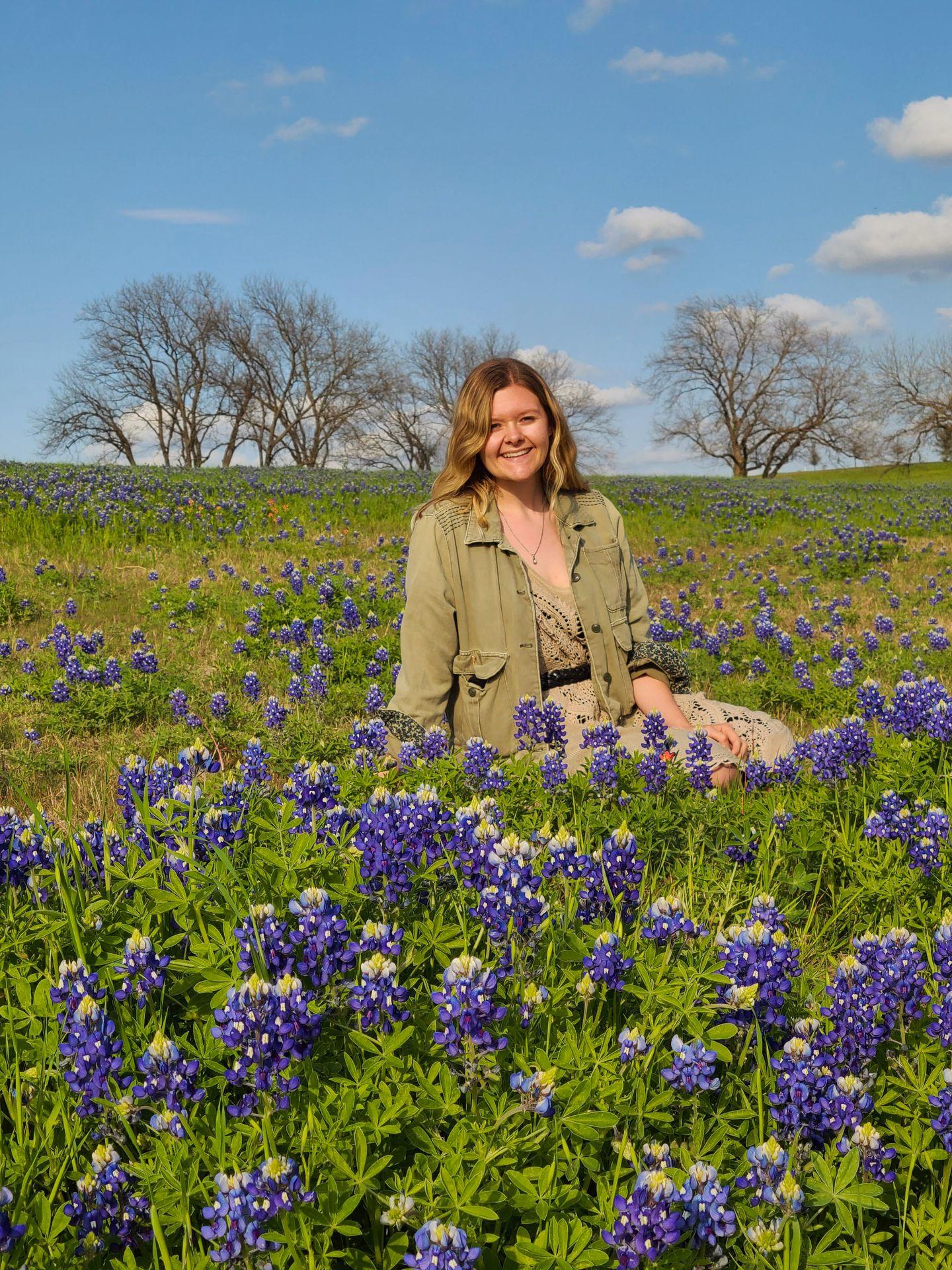 Lydia sitting behind some bluebonnets in a field.
