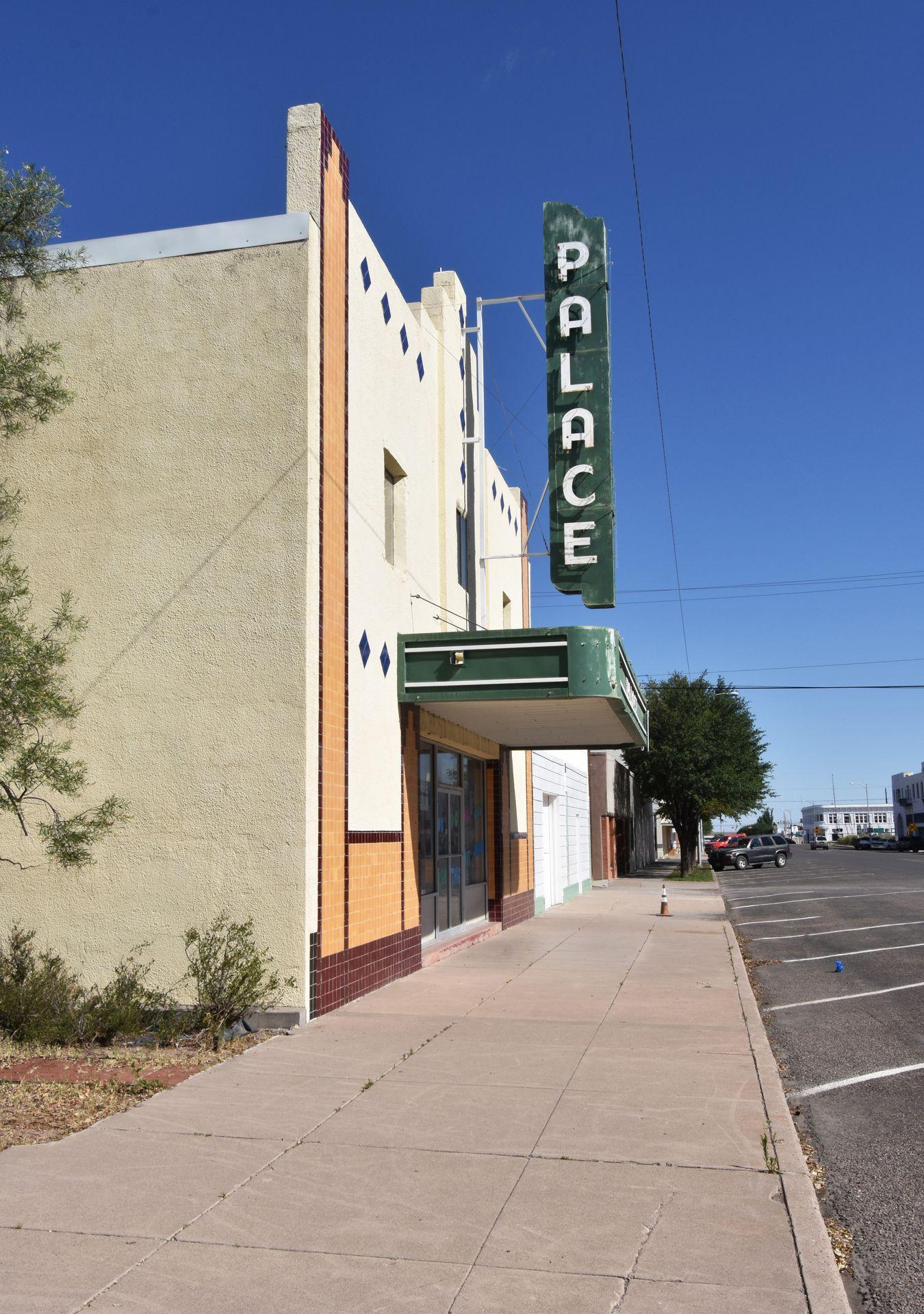 The exterior of the Palace theater. It is a white building with an orange design and a green sign.