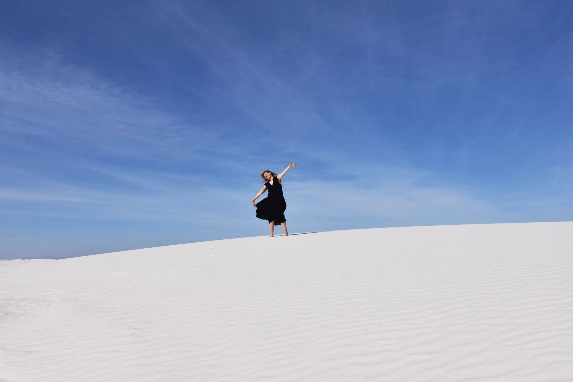 Lydia standing on top of a hill of white sand wearing a black dress.