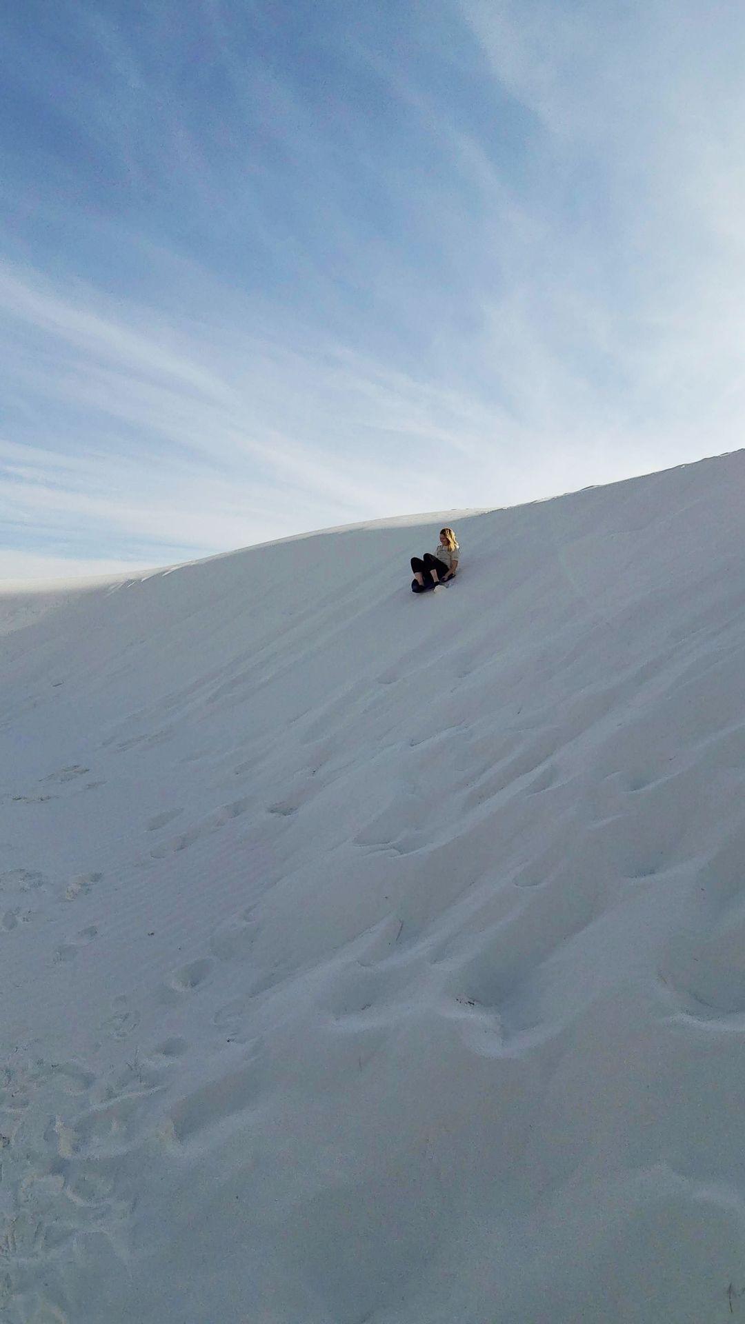Lydia sledding down a hill of white sand in the distance.