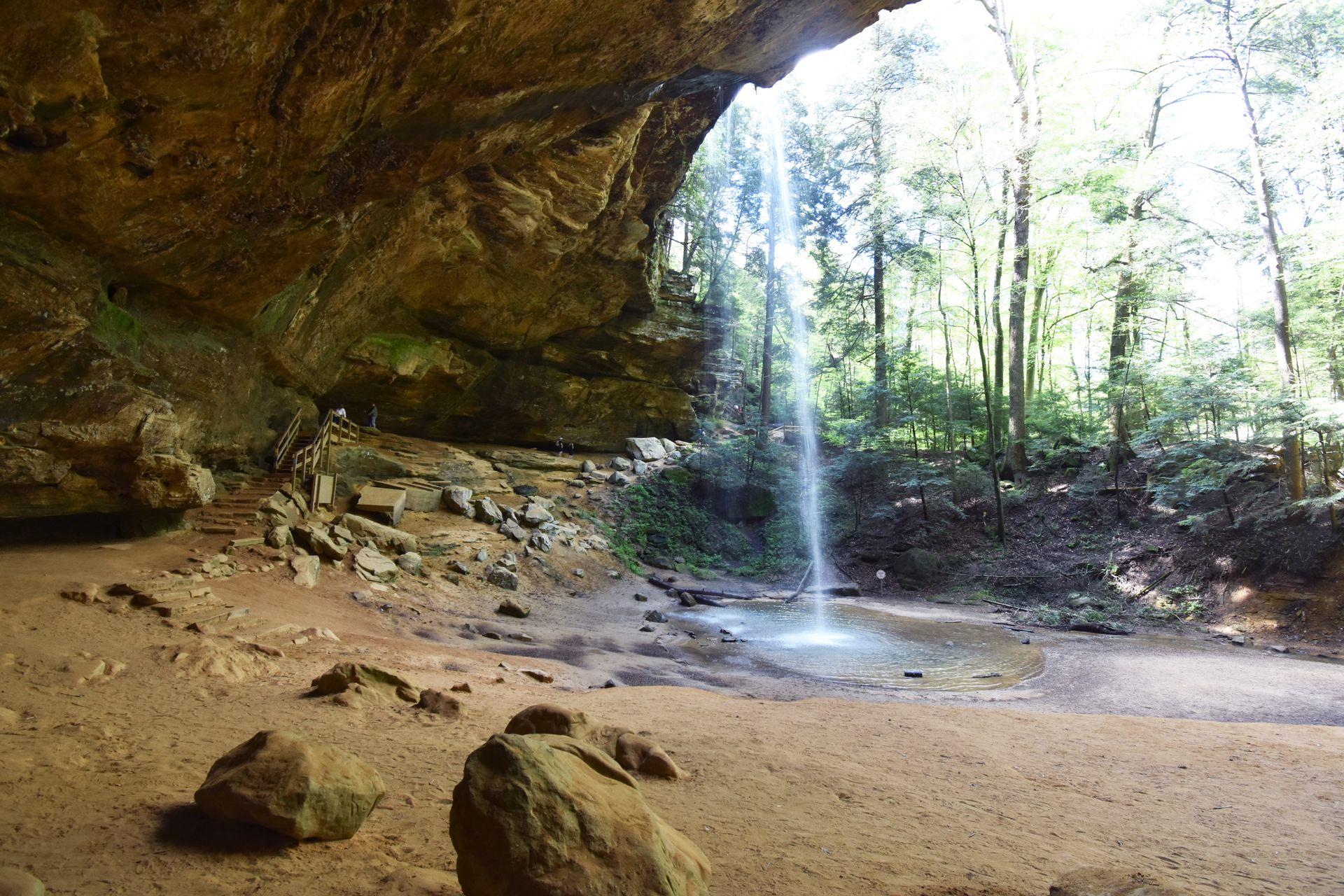 A view from inside of Ash Cave. There is a large overhang and a small waterfall coming off of the edge.