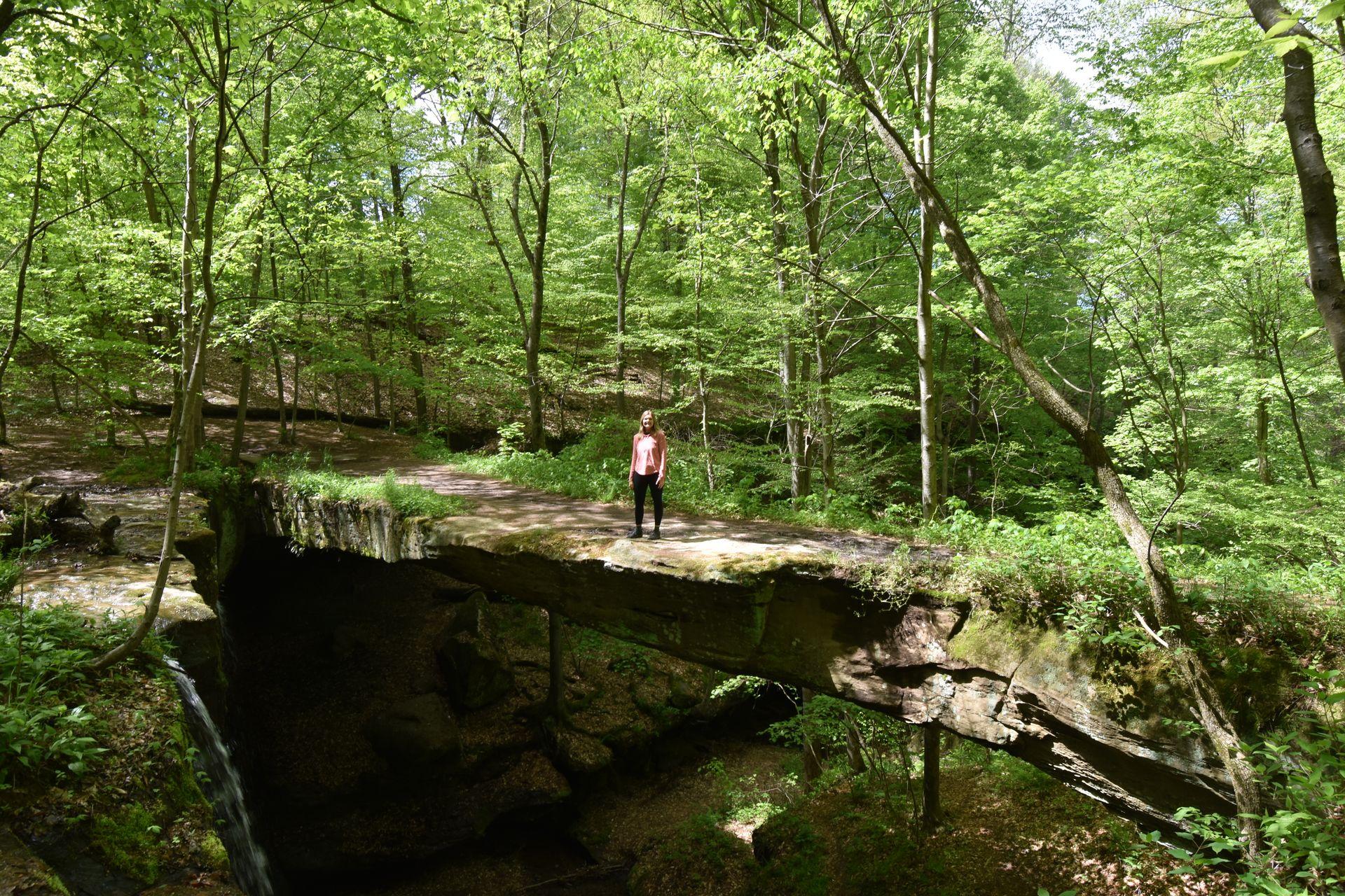 Lydia standing on a large natural bridge with trees in the background.