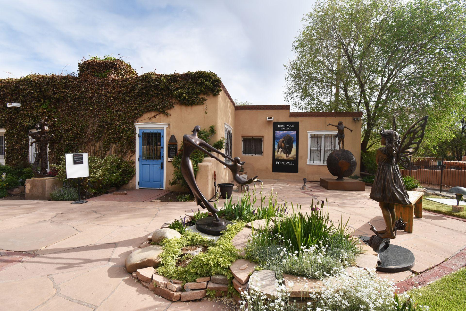 An art gallery on Canyon Road with several outdoor sculptures. The building is covered in vines and there is some beautiful greenery among the outdoor statues.