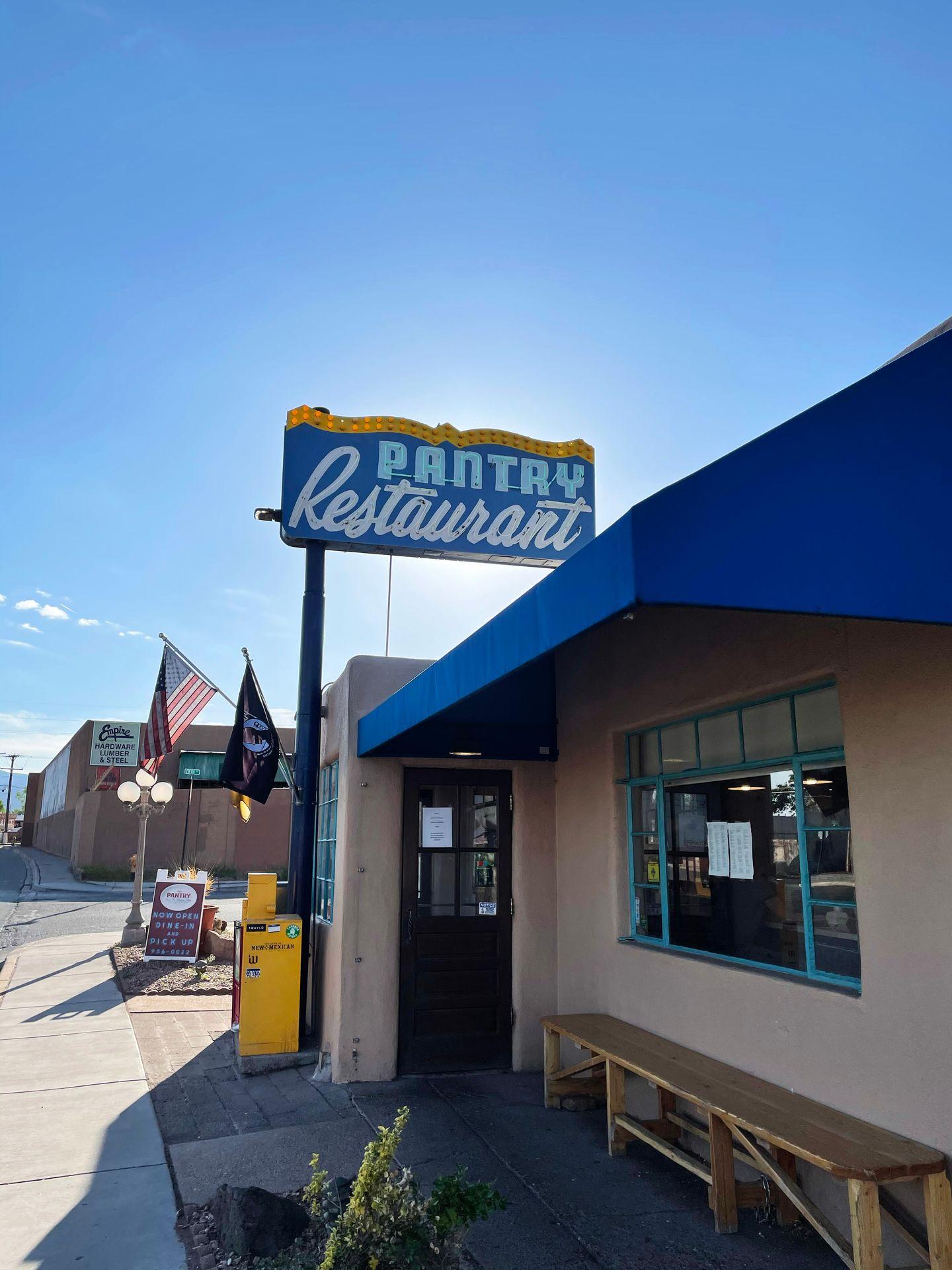 The exterior of The Pantry restaurant. There is a blue awning and a blue sign.