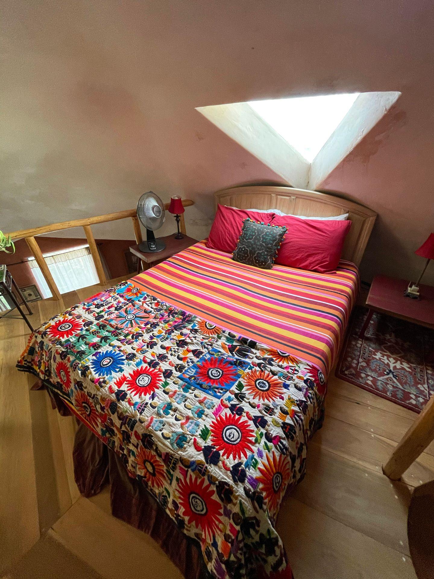 A colorful bed spread with a triangle shaped window above it inside the Dome House.