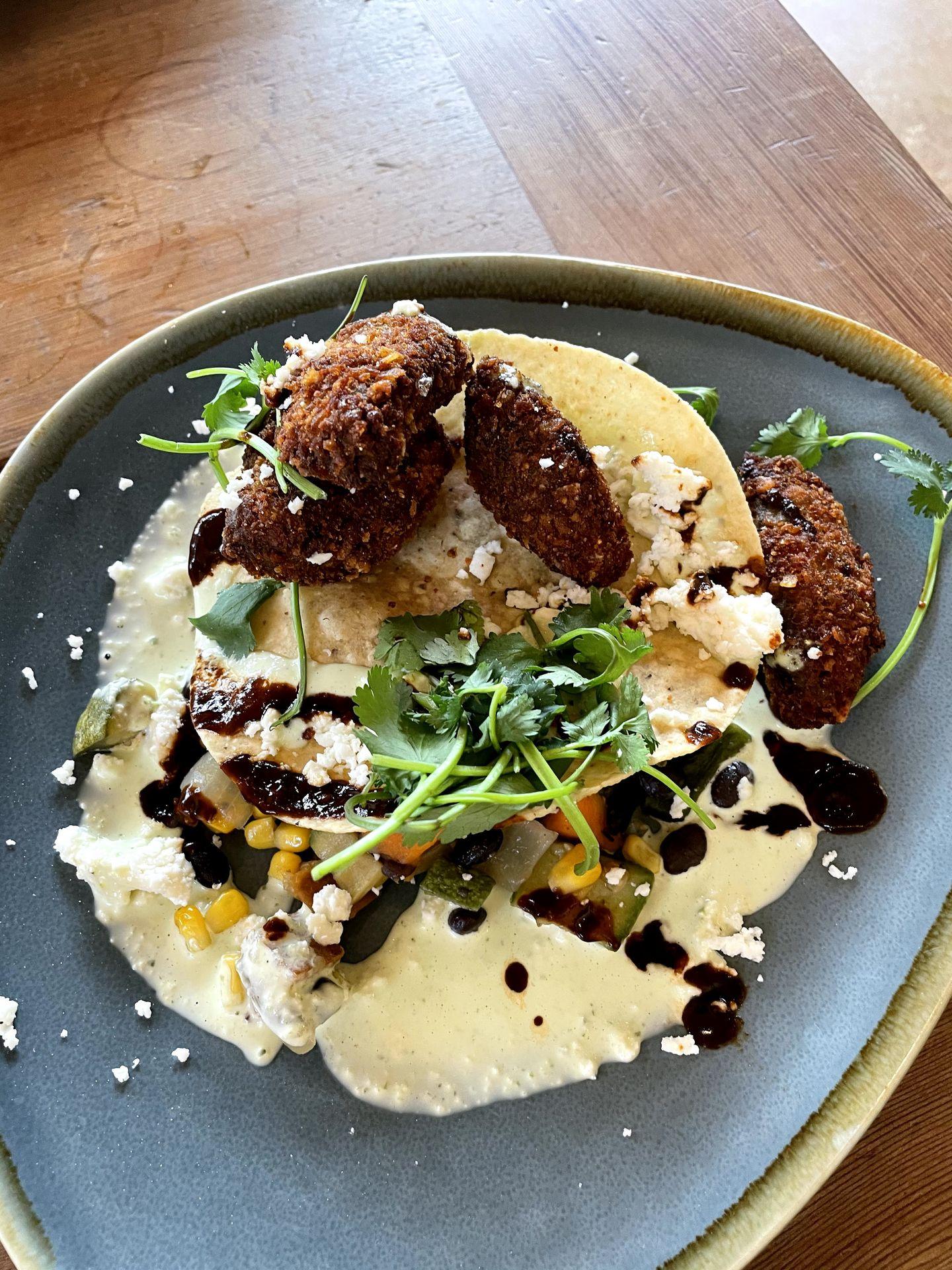 A plate with fried avocado, a sauce, corn, cheese and garnish from The Leaning Pear.