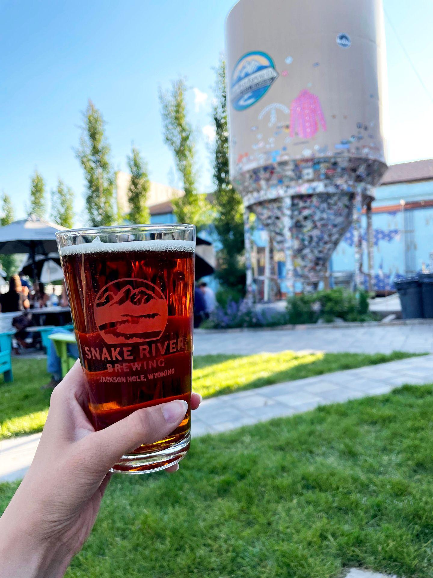 Holding up an amber colored glass of beer in the outdoor area of Snake River Brewing.