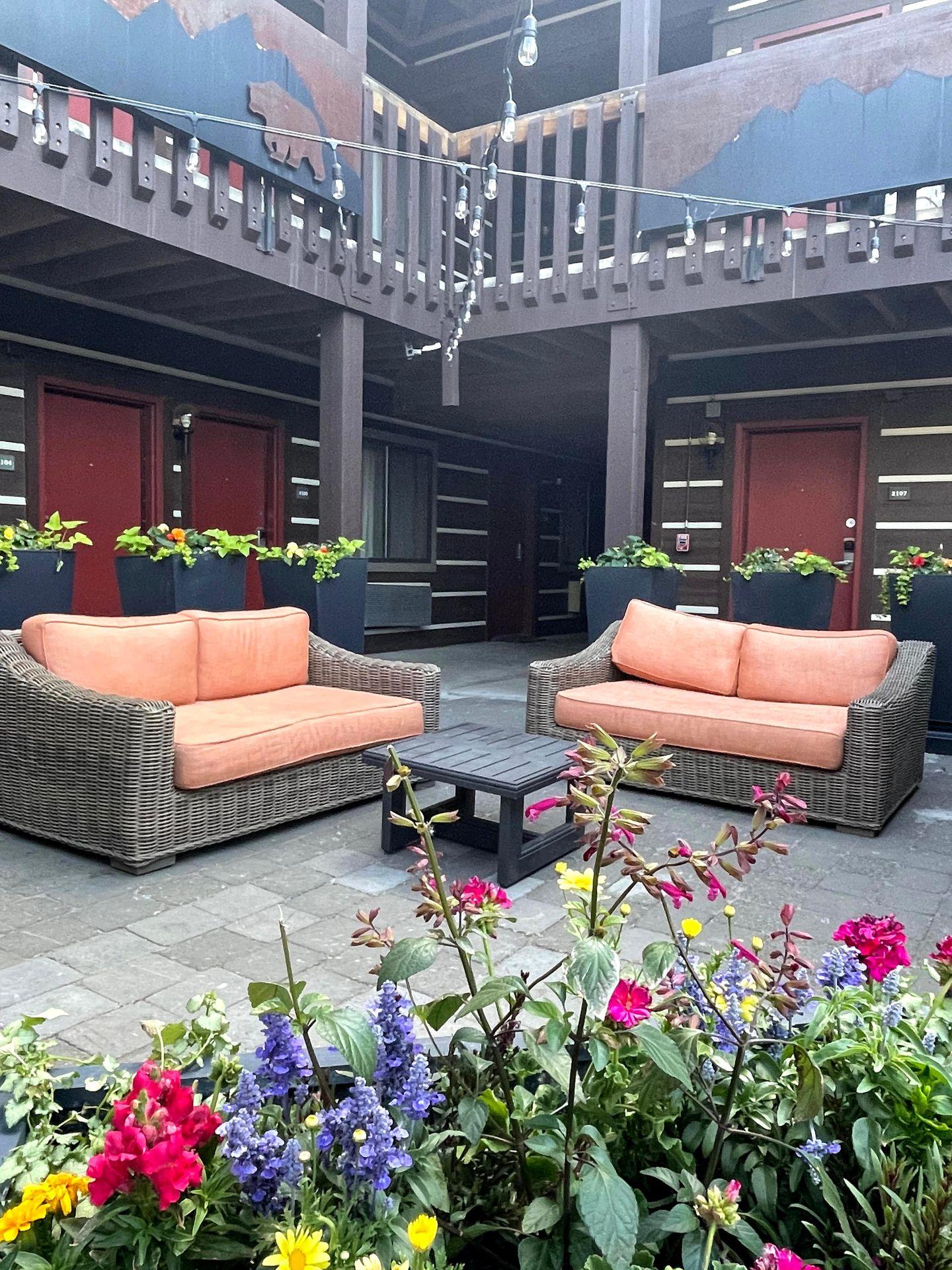 An outdoor seating area with two couches and a small table. It is surrounded by a display of colorful flowers.