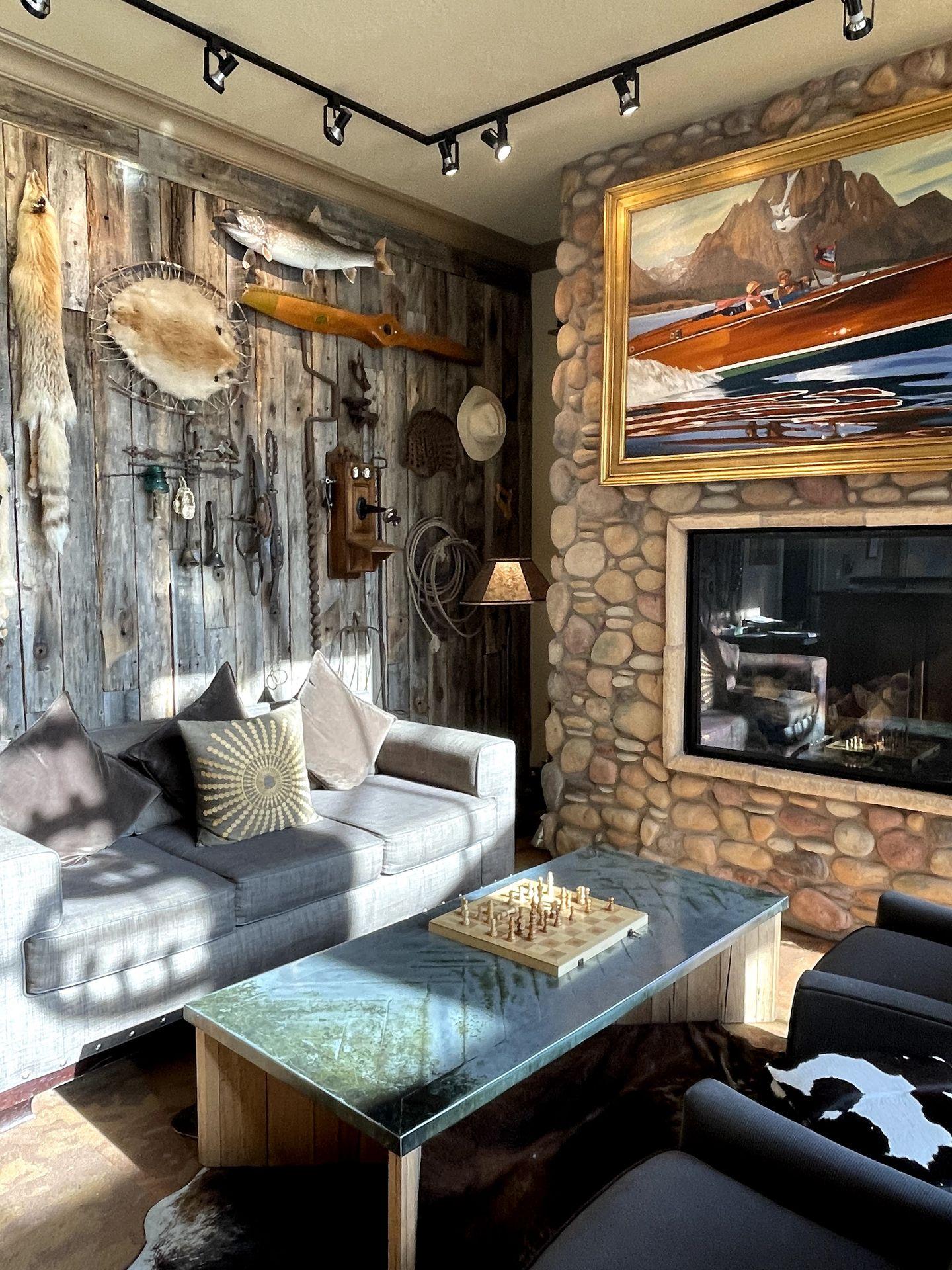 A corner of the lobby in Lexington Jackson Hole. There is a couch with throw pillows, a table with a chess set and a rustic wall with a fish, a hat, an animal skin and various outdoorsy decor.
