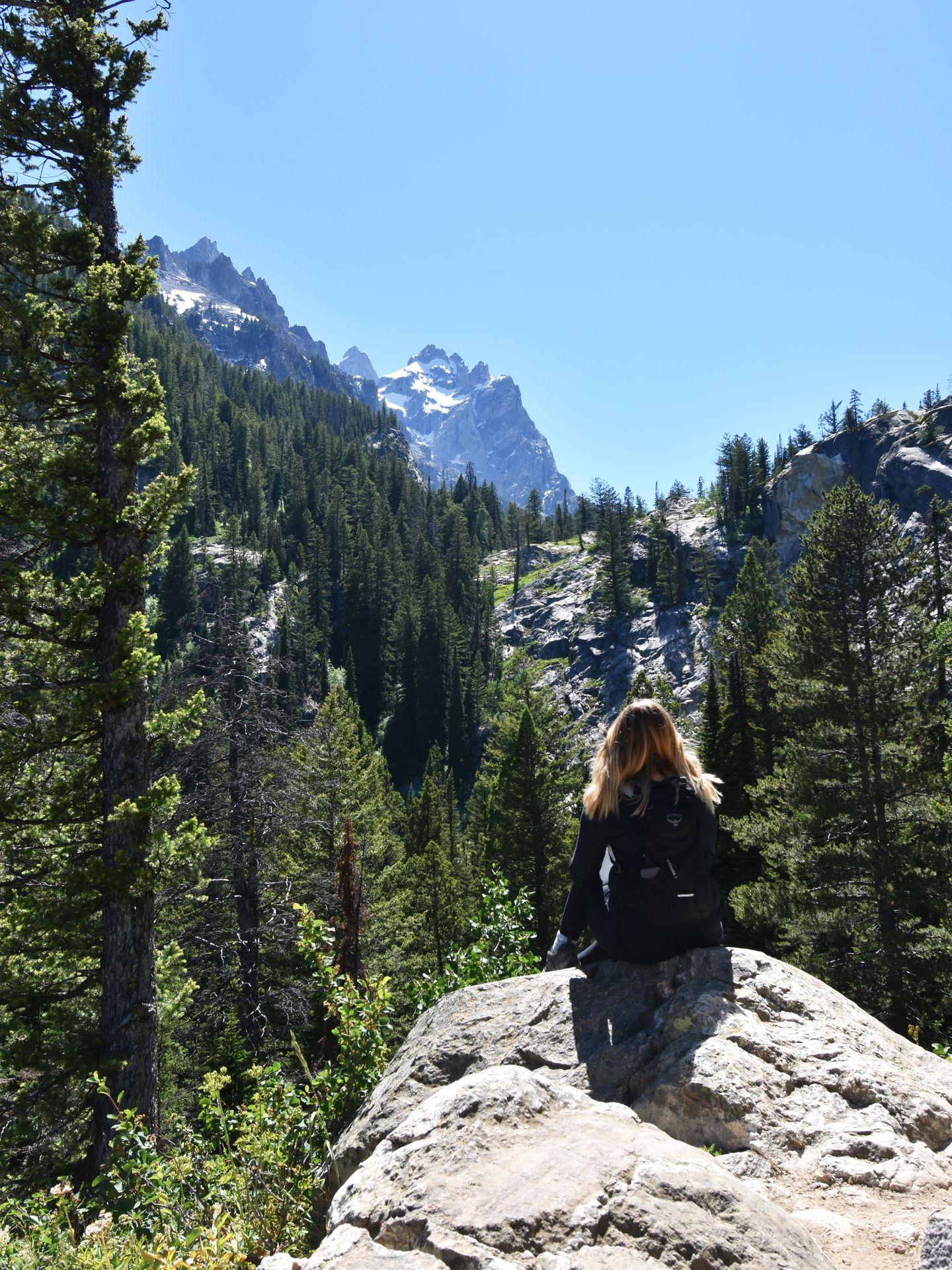 Lydia sitting on a rock looking out at a mountain view on the hike to Inspiration Point in Grand Teton National Park.