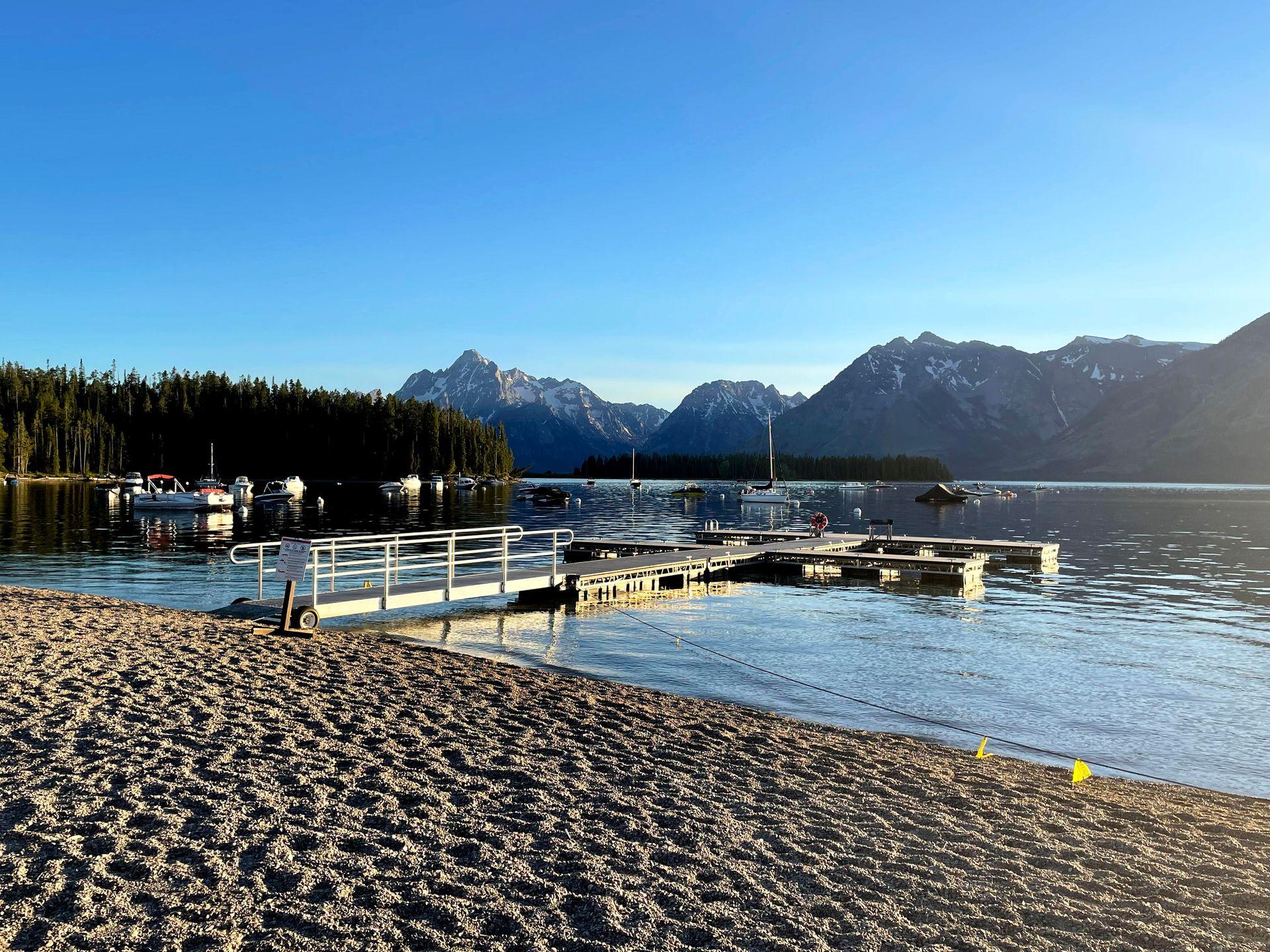 A dock extending out from a beach on Colter Bay Beach. There are several boats near the water.