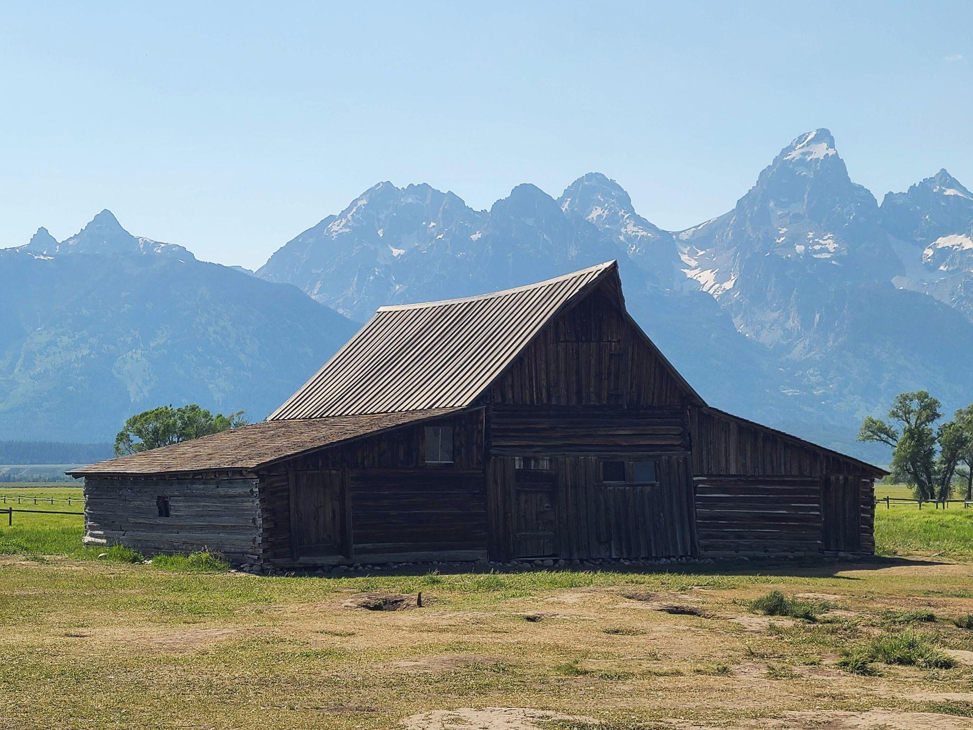 A log cabin with a pointed roof with mountains in the background.