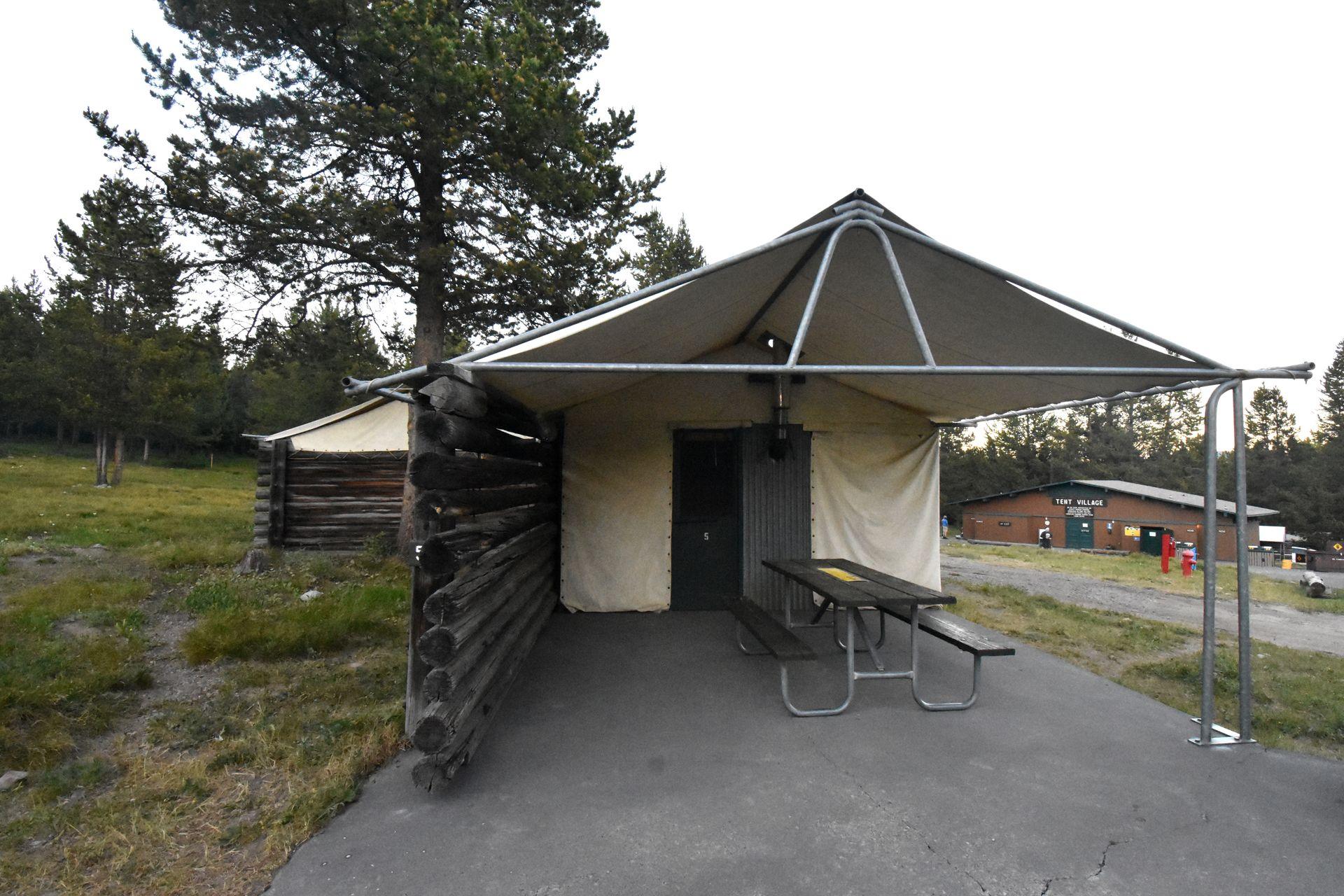 A safari tent at Colter Bay Tent Village. There is an overhang providing shelter in front of the tent and a picnic table.