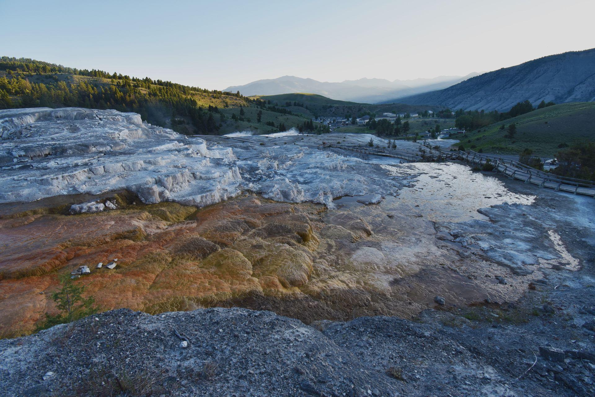 A view of orange and white hardened rock at the Mammoth Hot Springs. There are mountains in the distance.