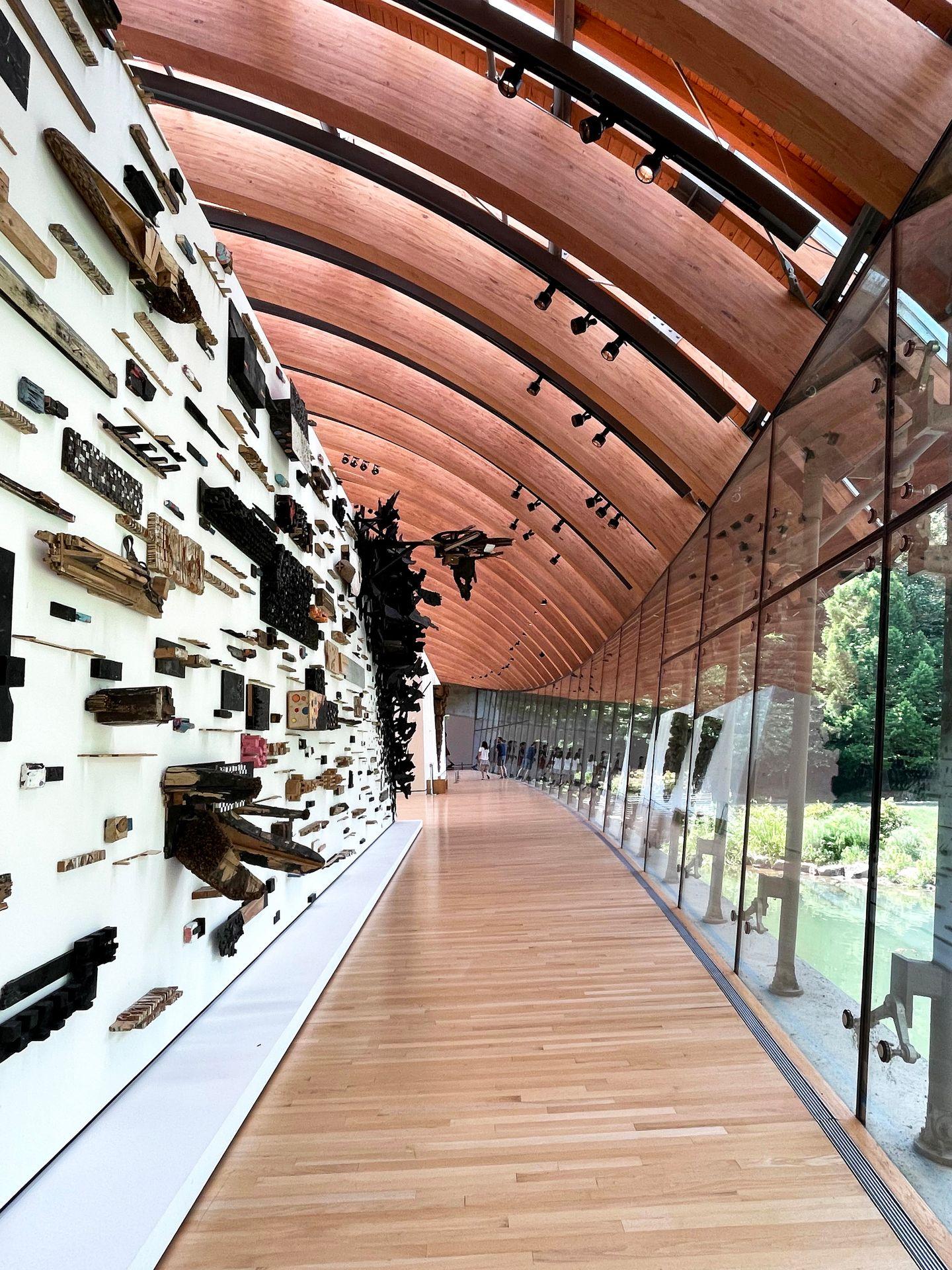 An open area in the Crystal Bridges Art Museum with art on the left on a white wall and a wall of windows on the right.