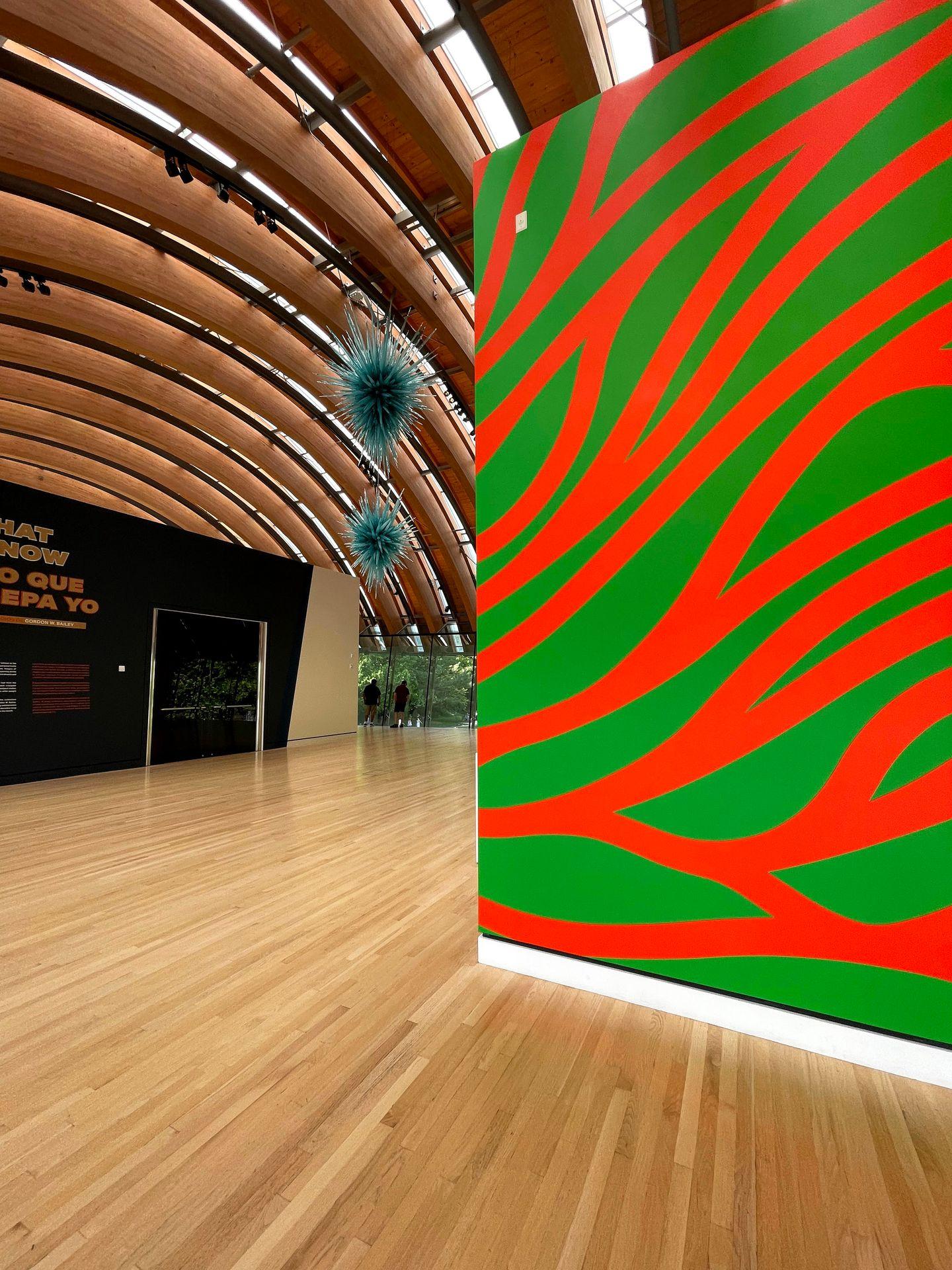 A neon red and green wall and a curved wooden ceiling inside of Crystal Bridges.