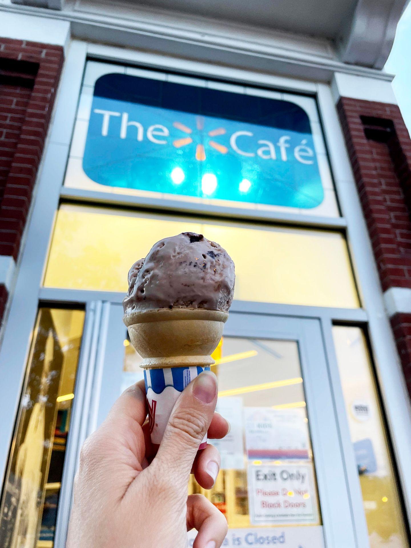 A scoop of chocolate ice cream in a cake cone in front of the Walmart Cafe