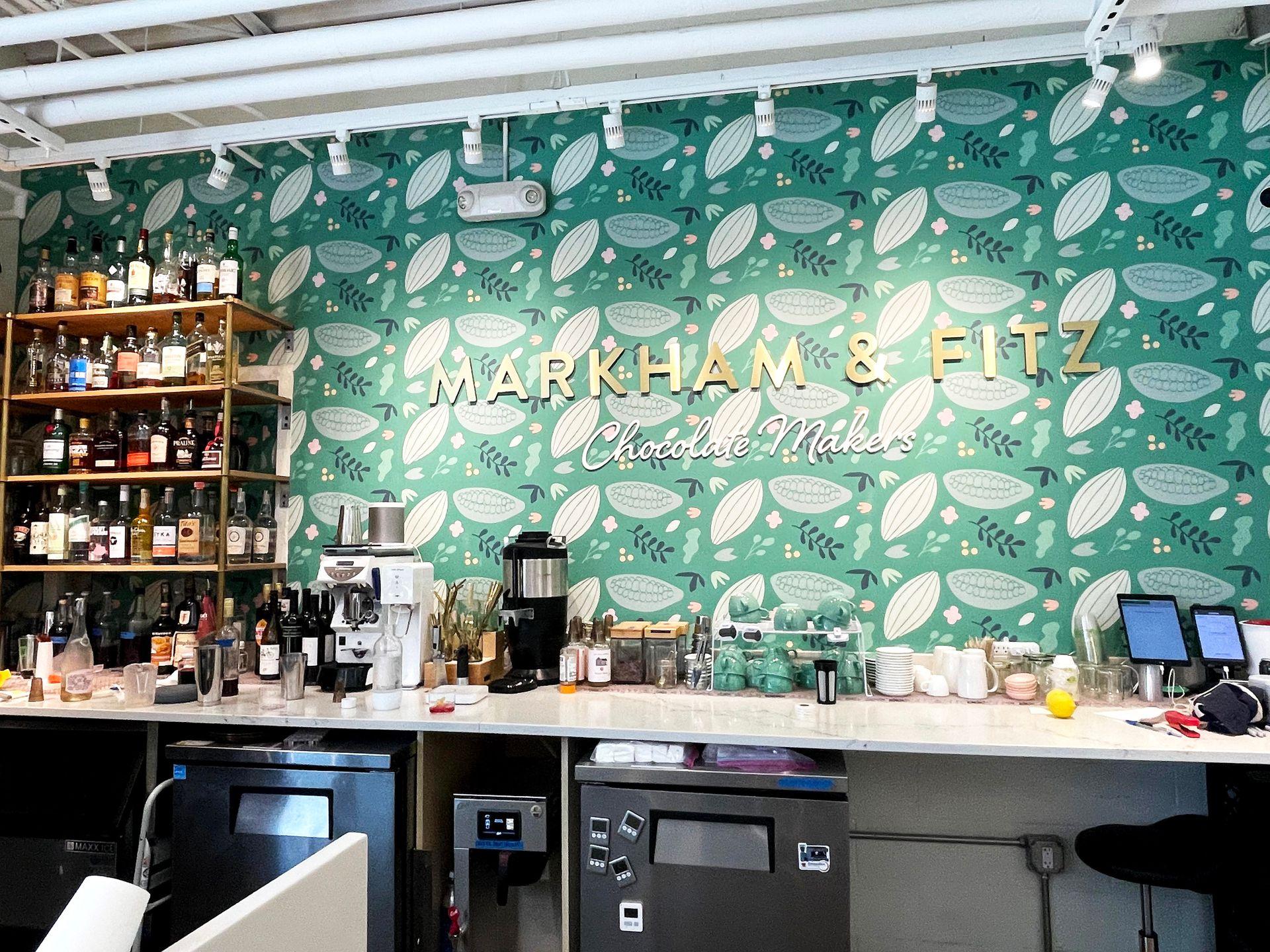 A green wall with a cocoa bean design behind the counter at Markham and Fitz.