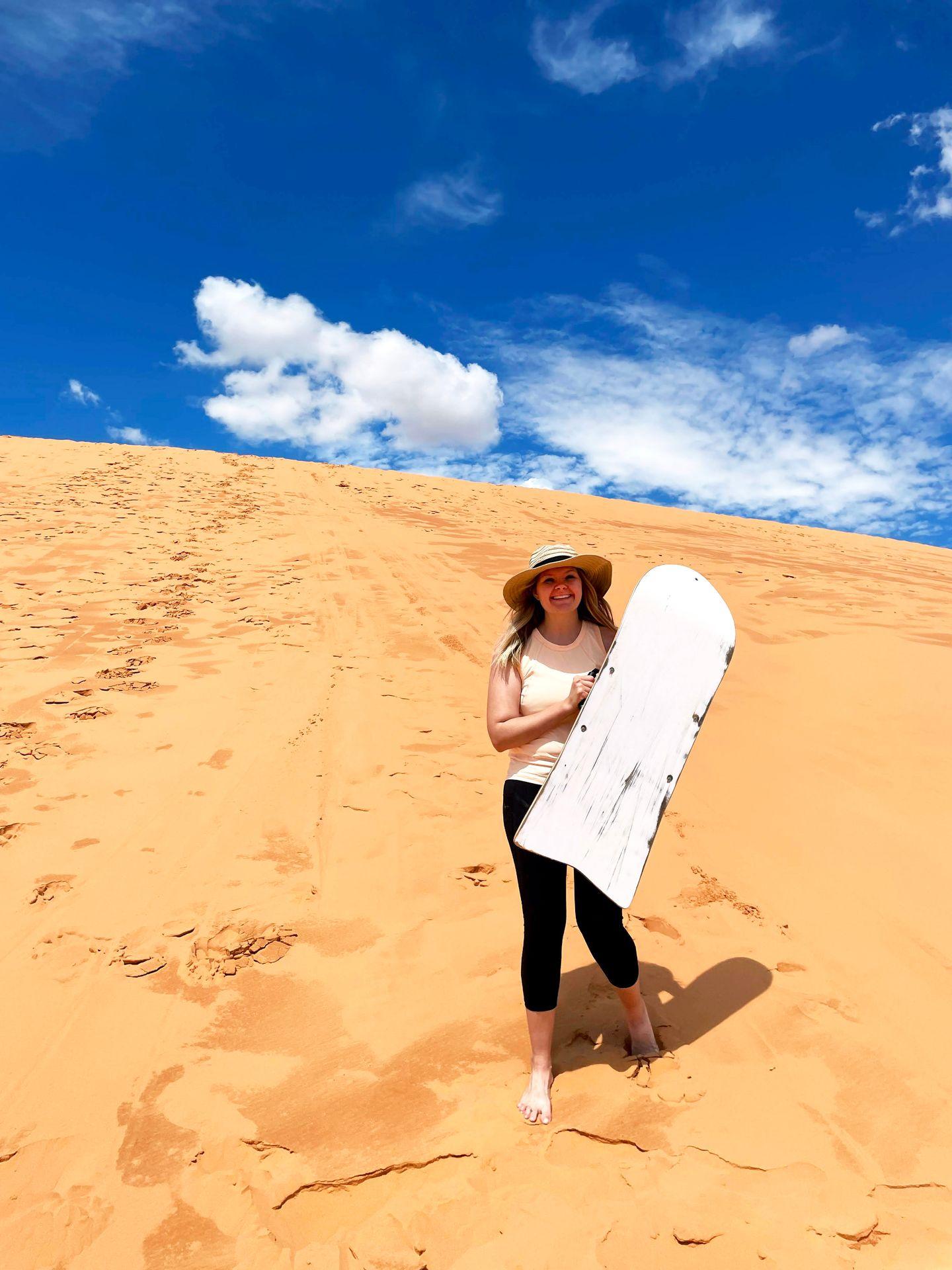 Lydia holding a sand sled at Coral Pink Sand Dunes.