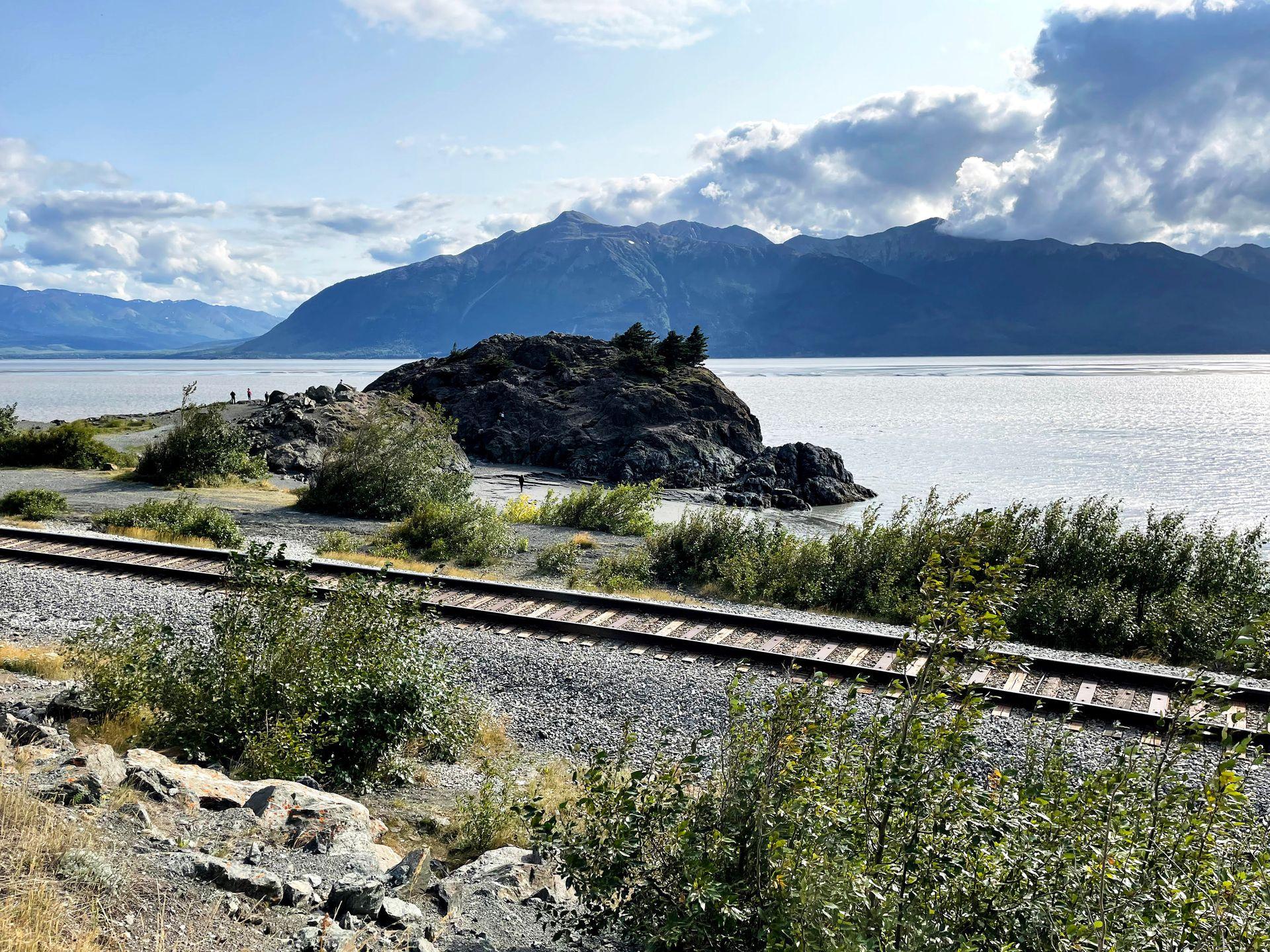 Train tracks and a giant rock on the water along the Seward Highway.