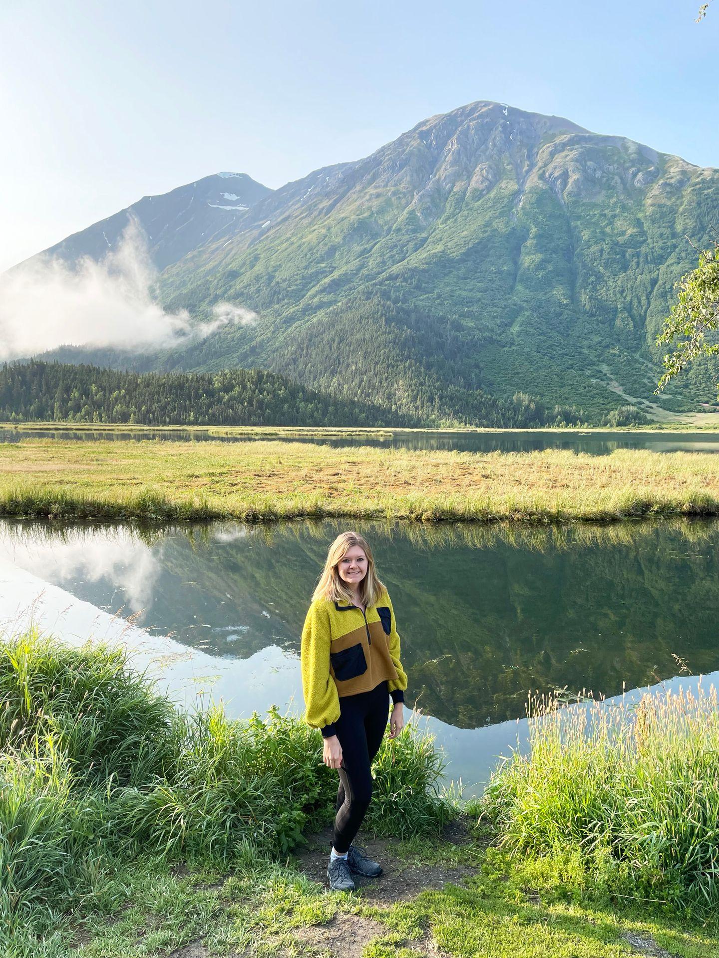 Lydia standing in front of Tern Lake, which has a beautiful mountain reflection on the water.