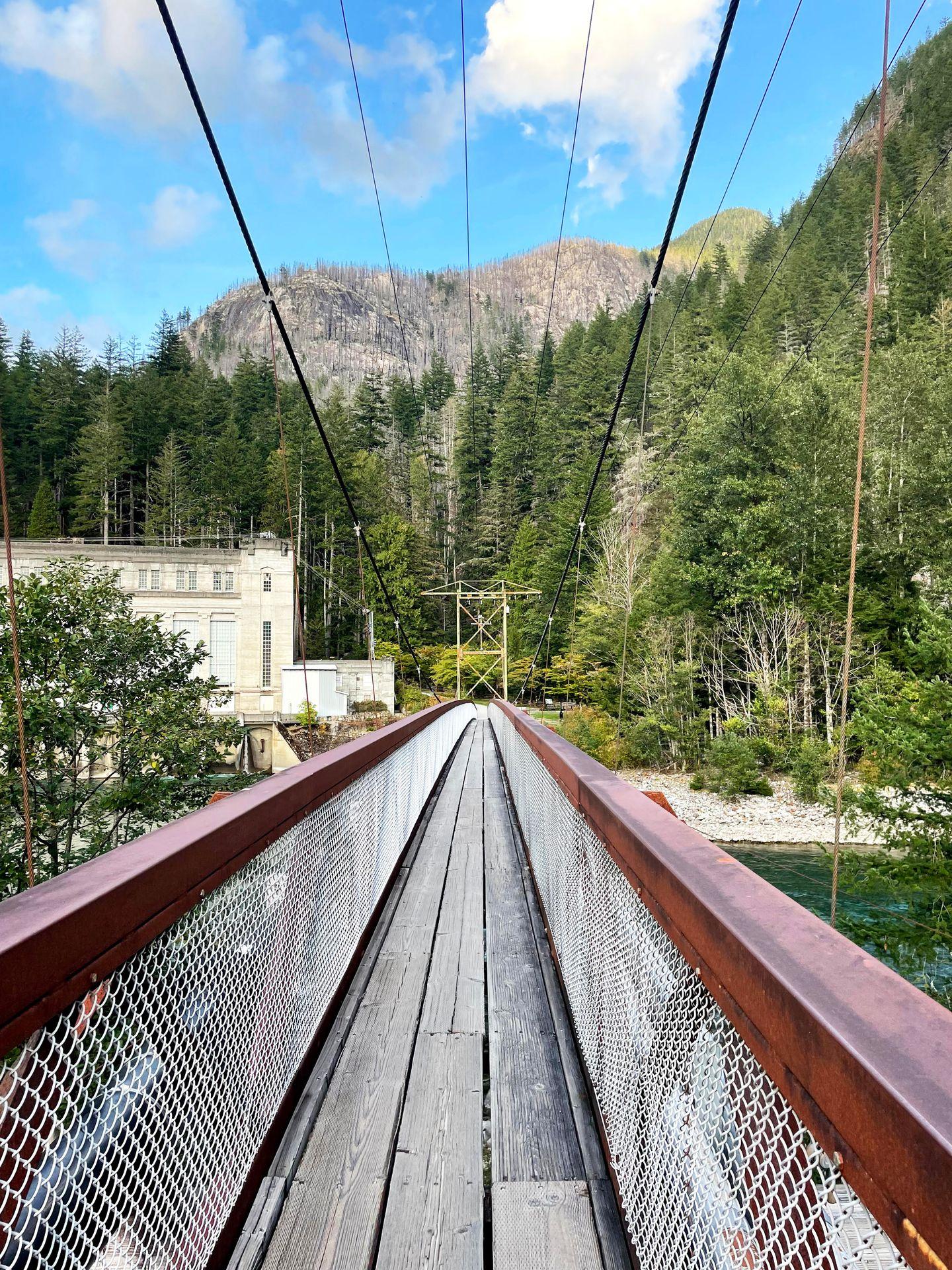 Looking across the Suspension Bridge in Newhalem. Across the bridge there are trees and mountains.