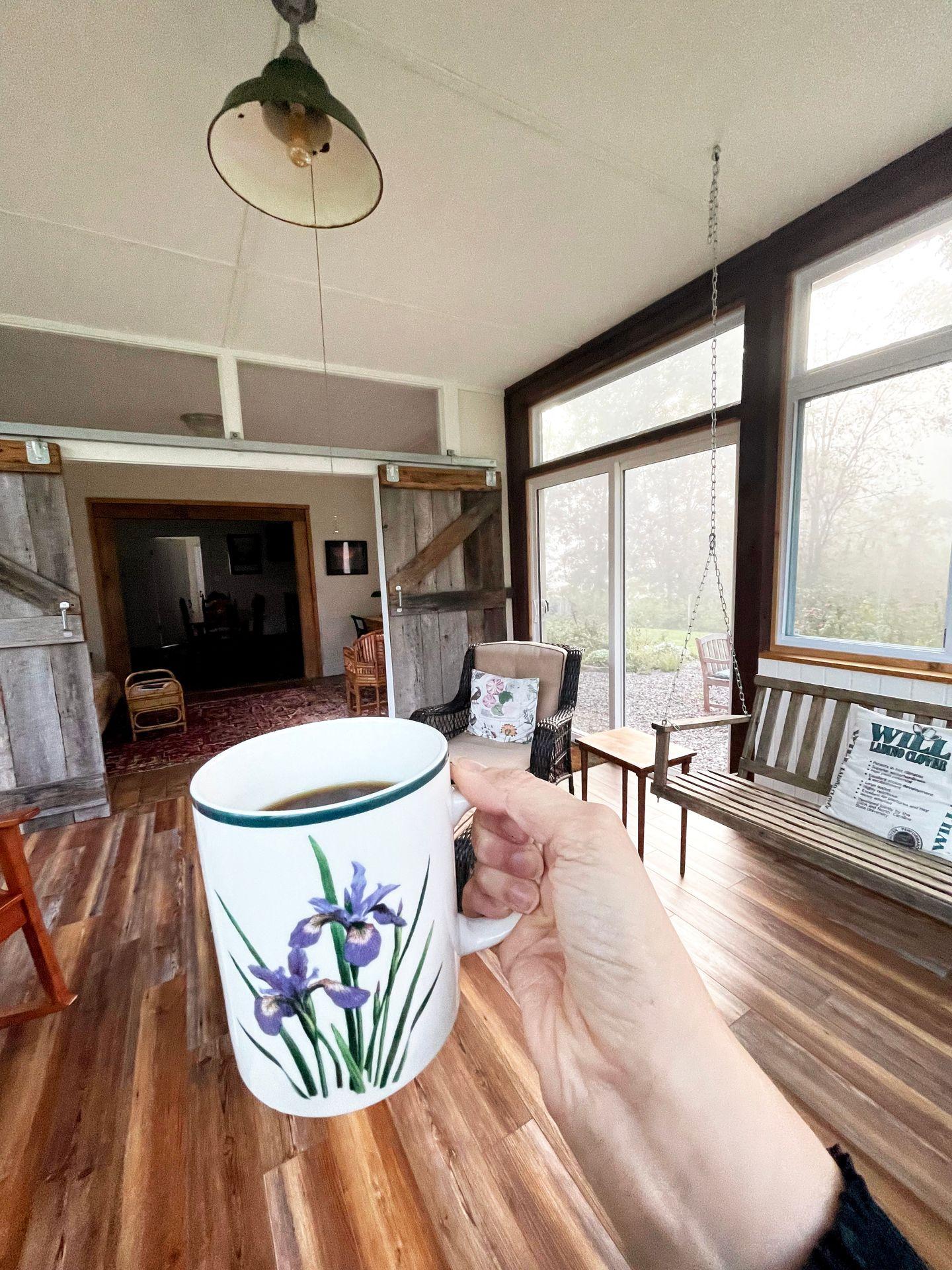 Holding a coffee mug with a purple flower inside of Five Springs Farm airbnb.