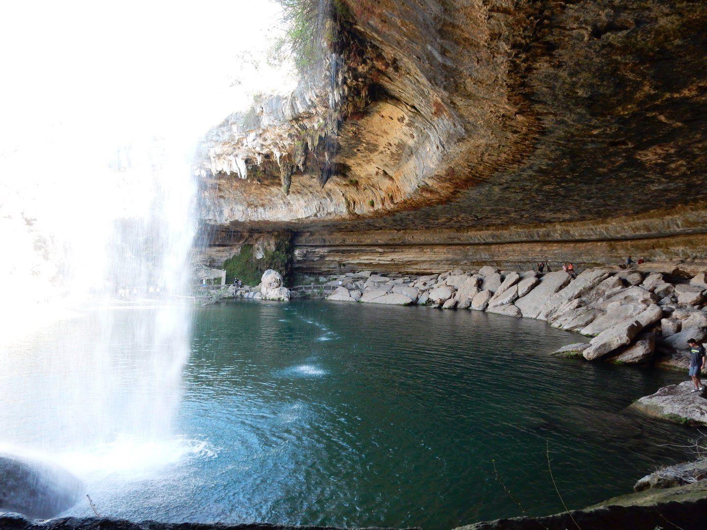 The large alcove of Hamilton Pool Preserve. Water cascades over the rim and into the pool of water below.