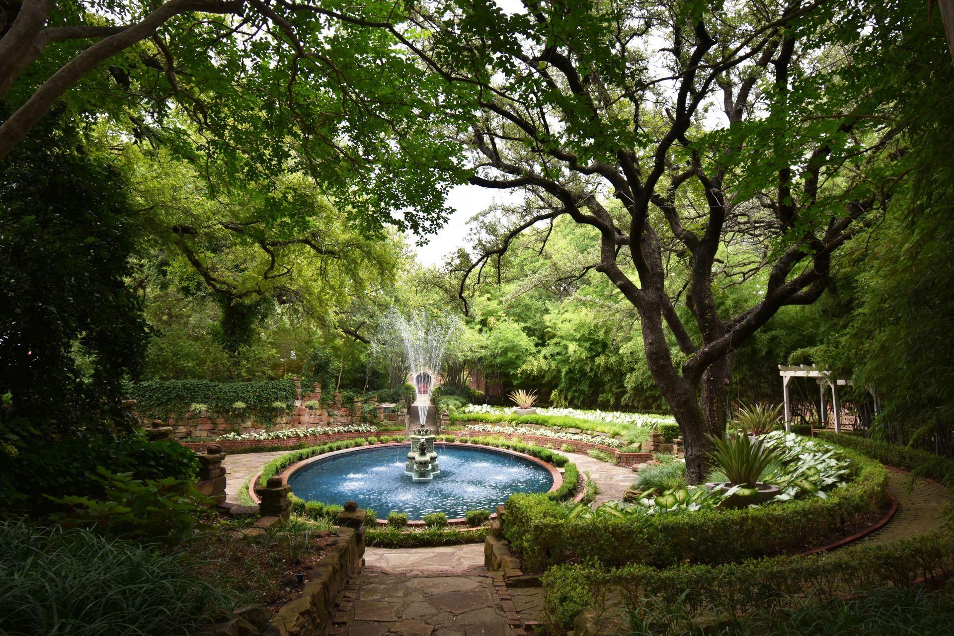 A blue fountain surrounded by green hedges and trees at Chandor Gardens.