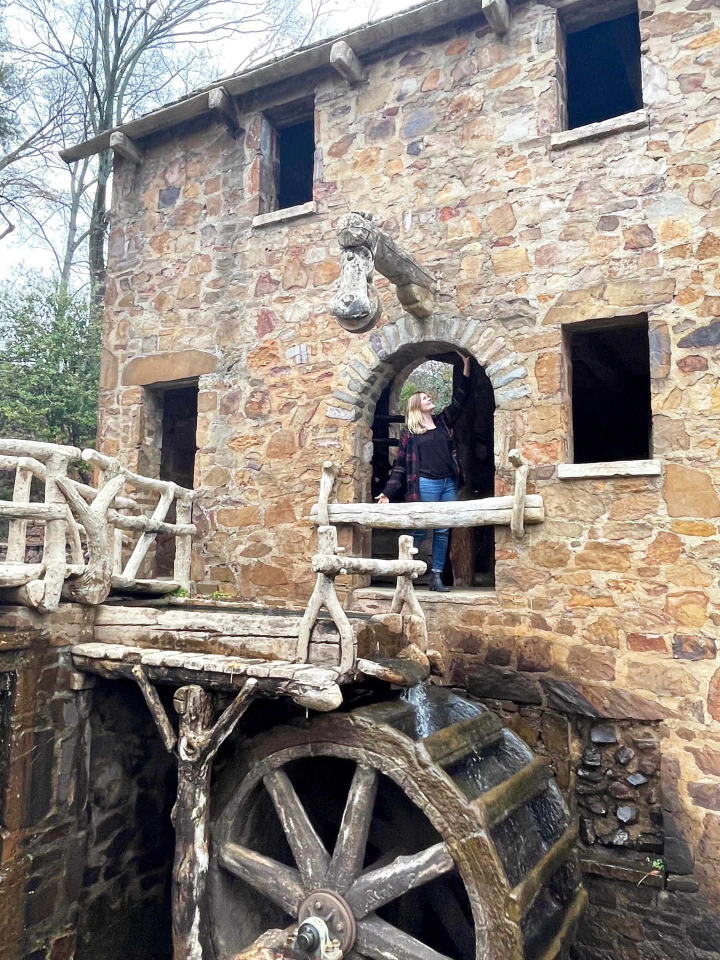 Lydia standing in the archway of the Old Mill. The building is made of tan stones and the water mill is below.