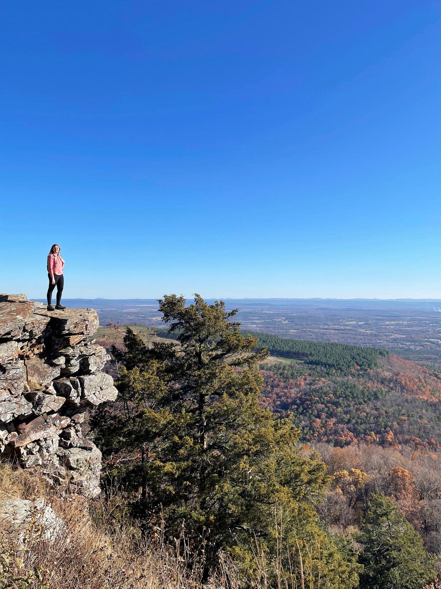 Lydia standing on the edge of rocky cliff with a view of a valley in the background.