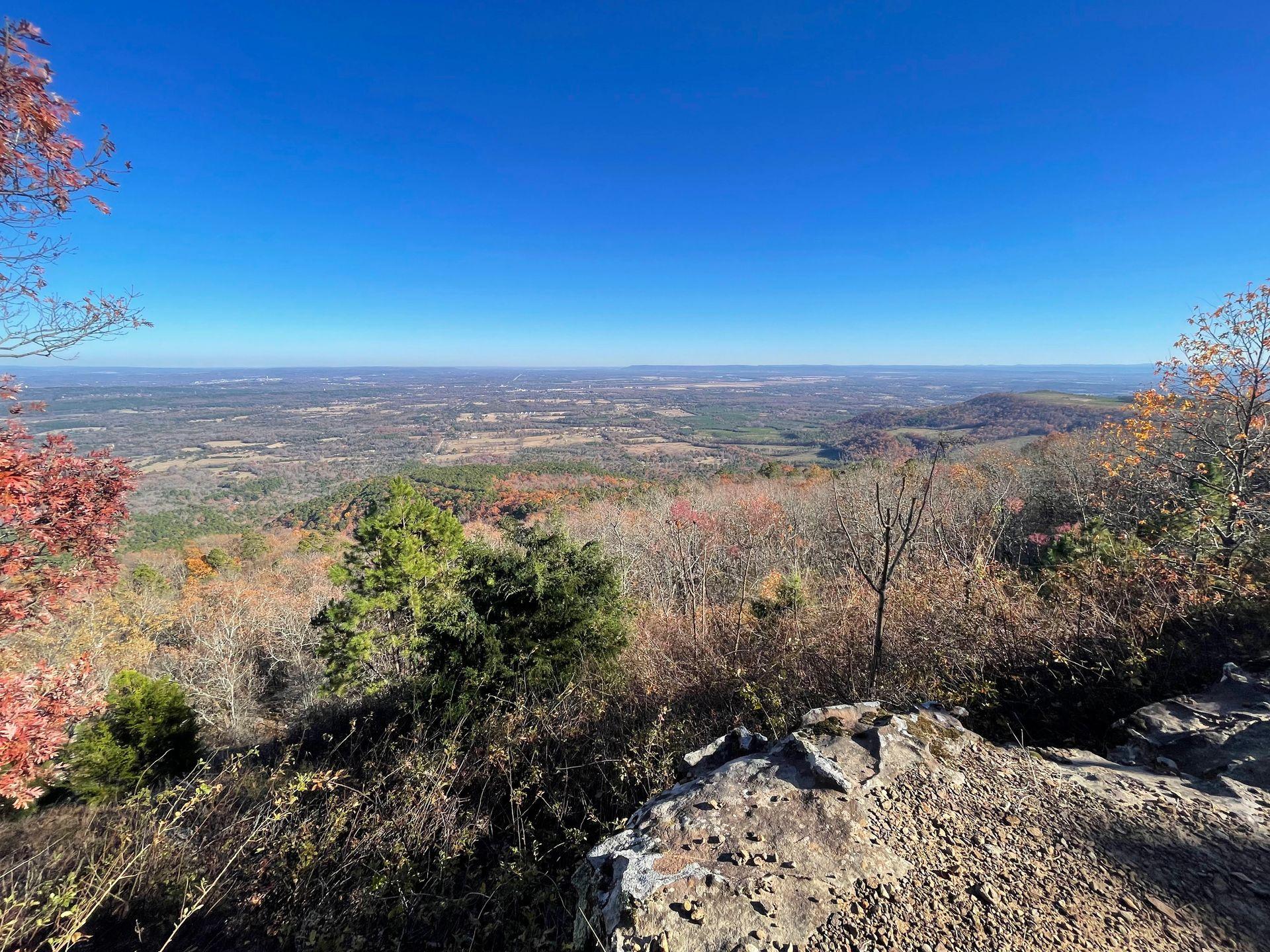 Looking down at a valley from Rim trail in Mount Nebo State Park. There are bits of colorful fall foliage mixed throughout the landscape.