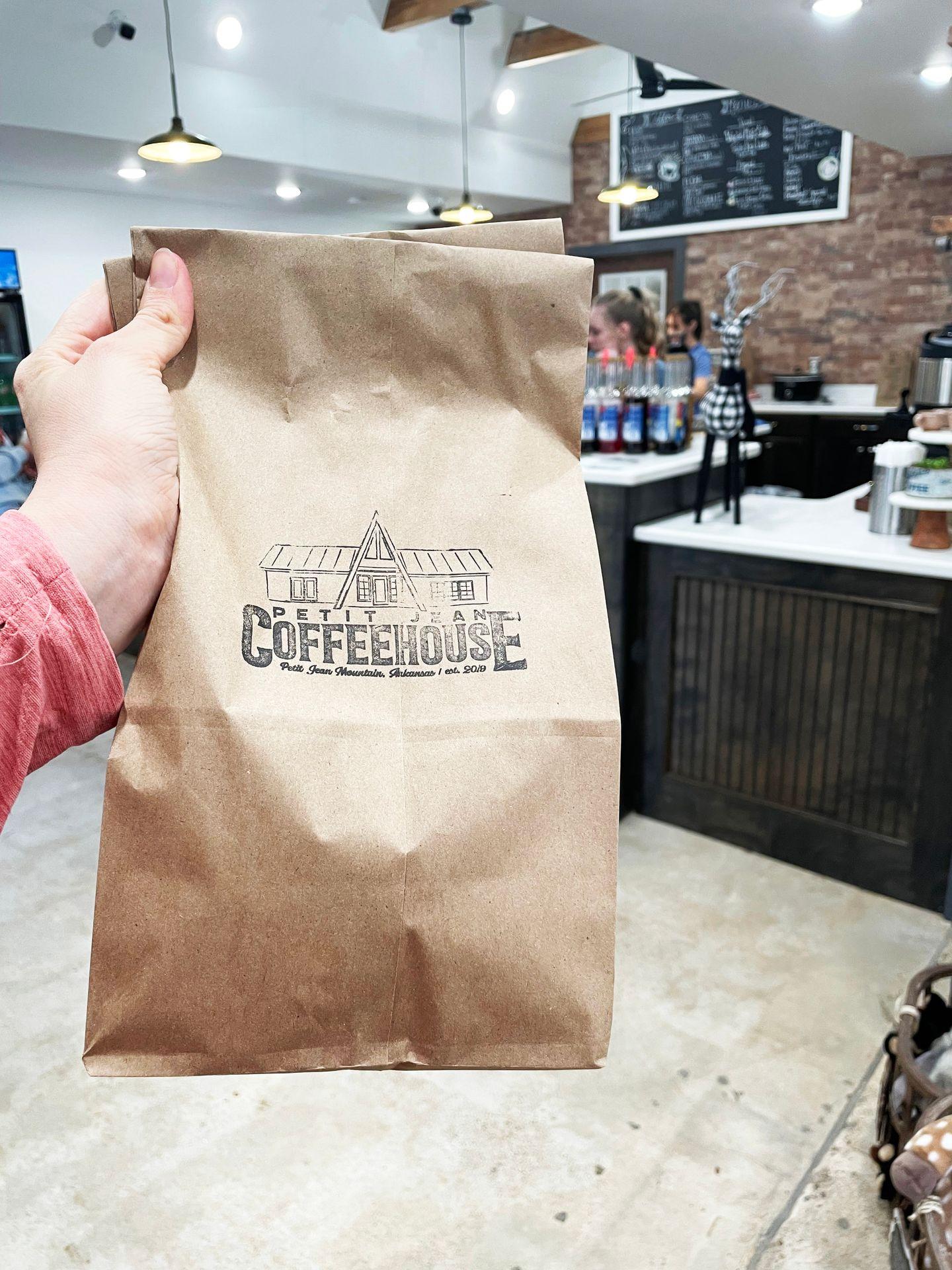 Holding up a brown paper bag that is stamped with the Petit Jean Coffeehouse logo