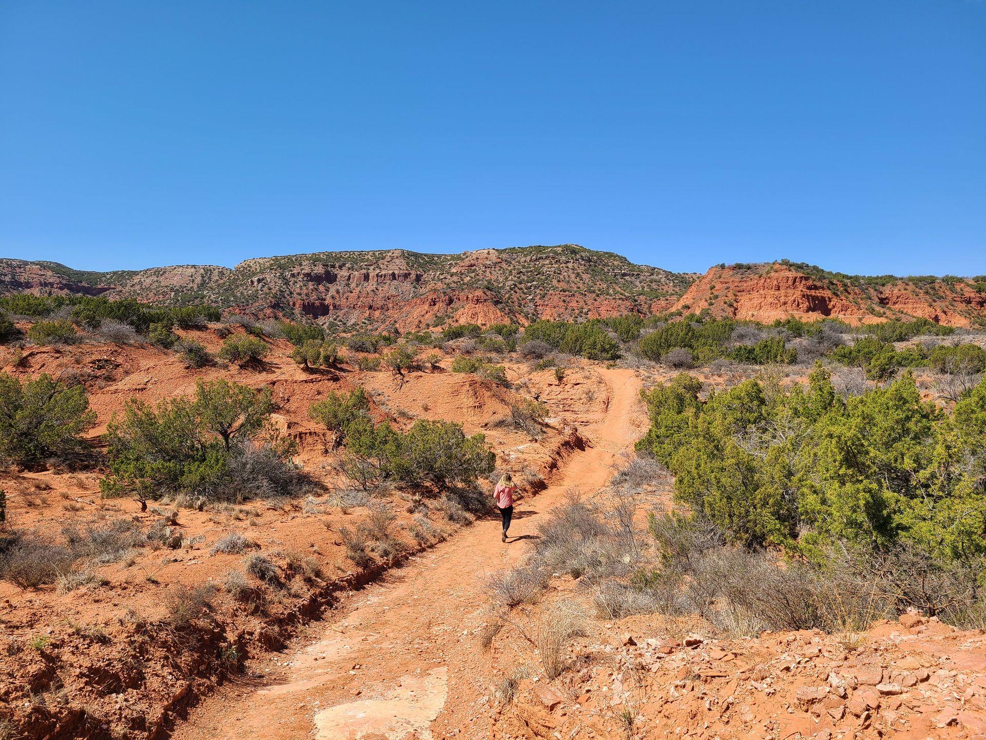 Lydia hiking on a trail surrounded by orange rocks at Caprock Canyons State Park.